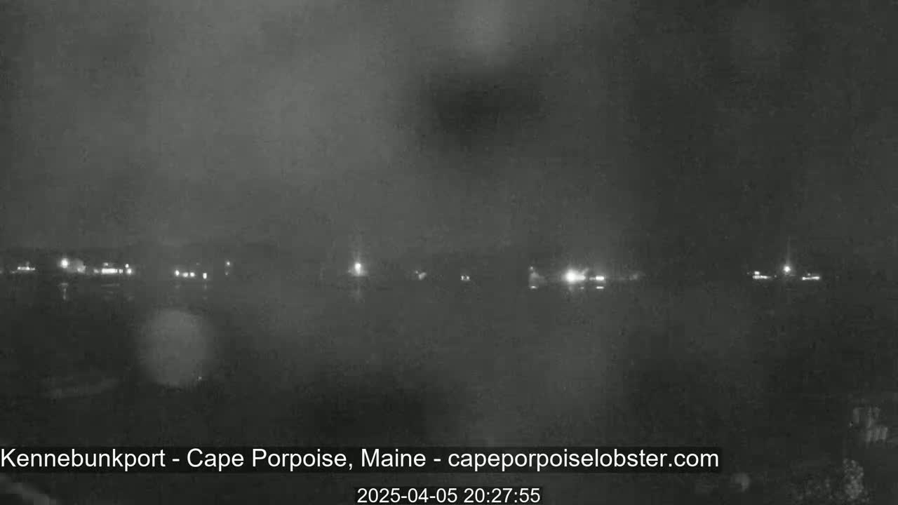 A nighttime, low-visibility view shows a distant shoreline with scattered lights under a dark, overcast sky.