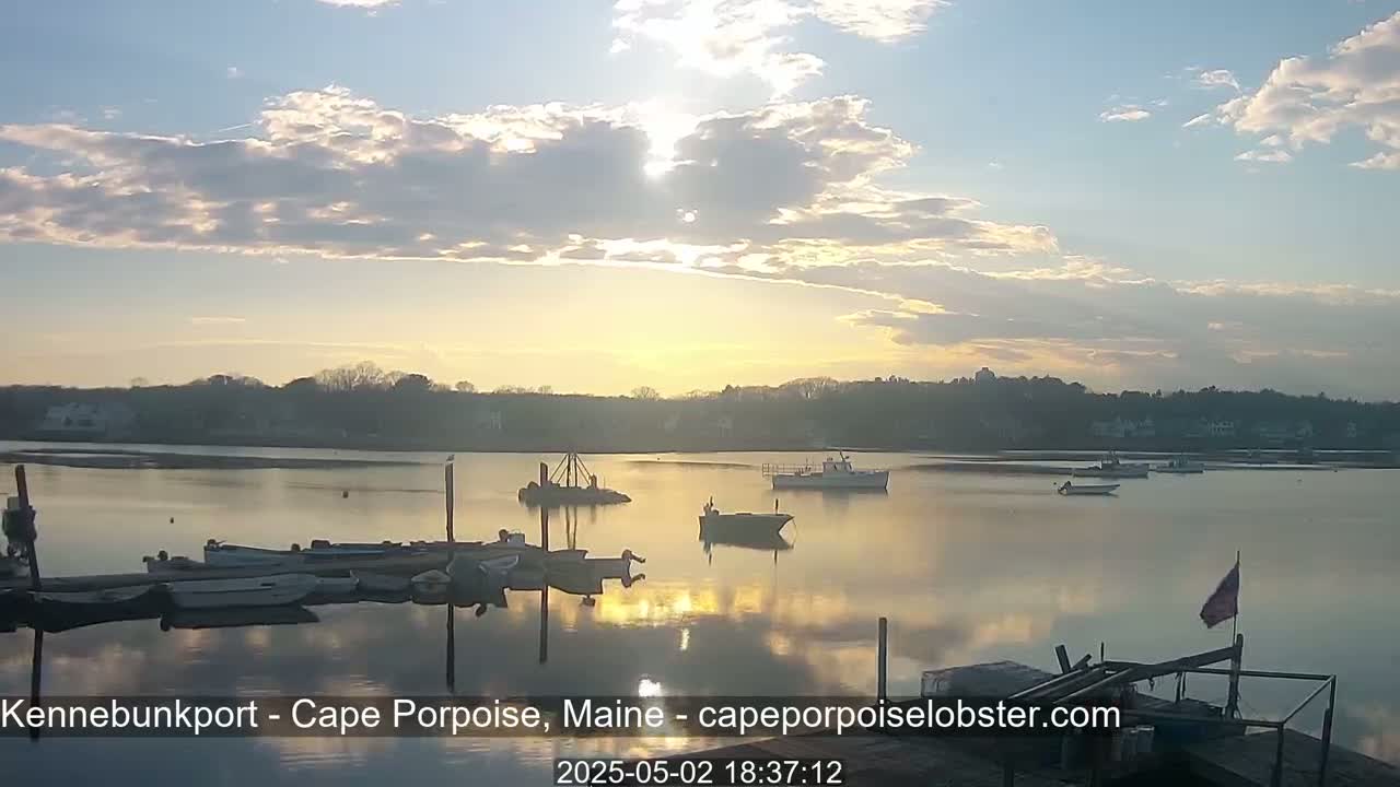 Several boats are moored at a dock on a calm body of water under a partly cloudy sunset sky.