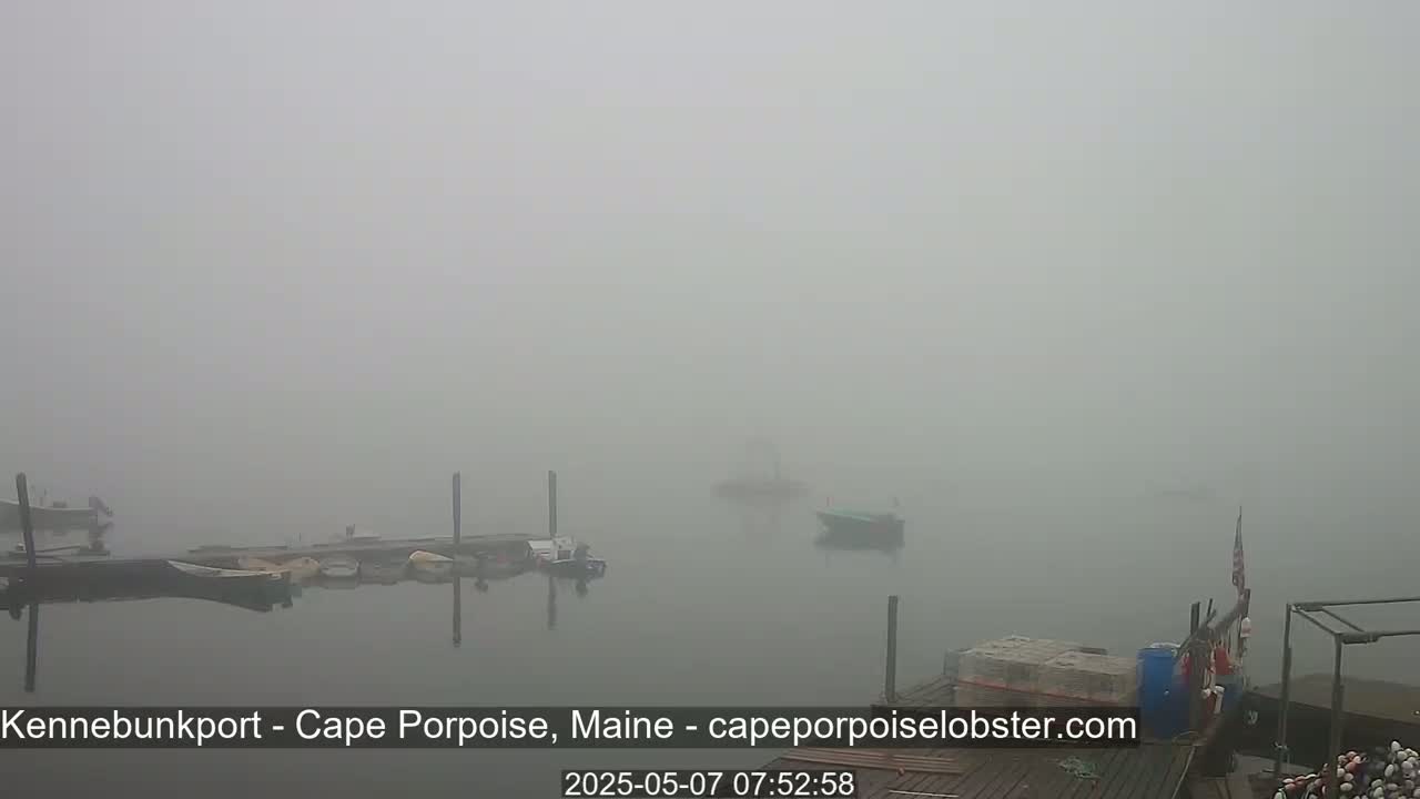 Several small boats are moored at a dock in a thick fog.