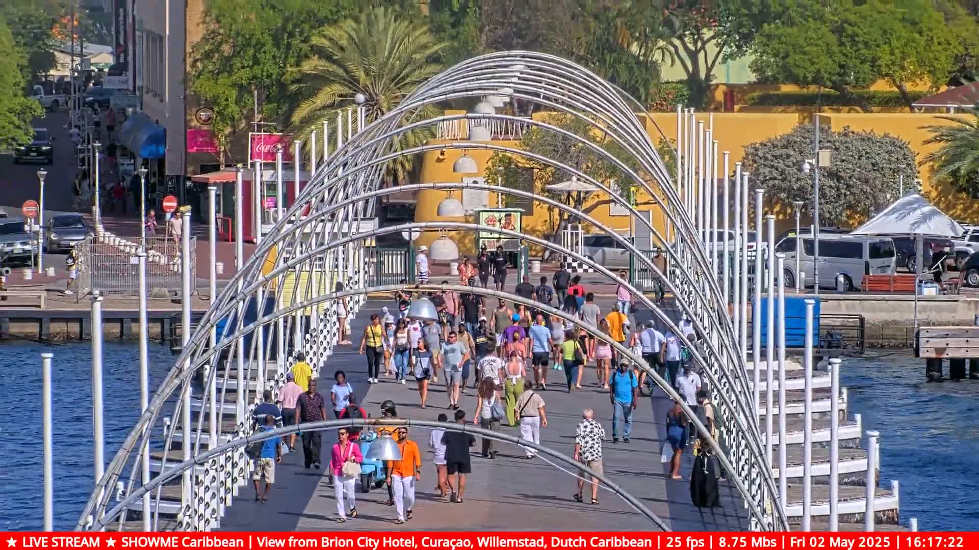 A long, curved pedestrian bridge with many people walking on it under a sunny sky.