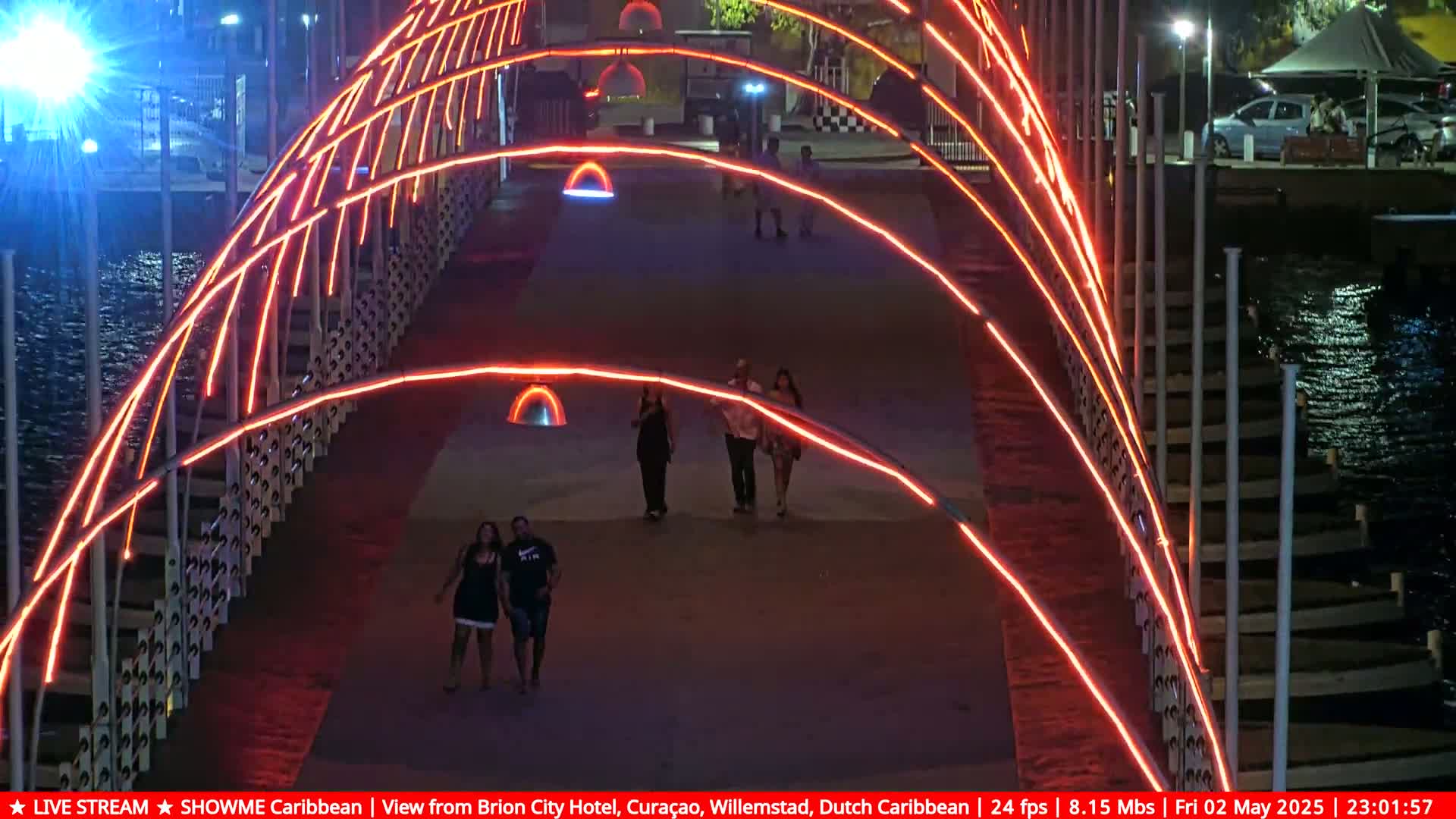 A bridge at night, illuminated with bright orange lights, has several people walking across it.