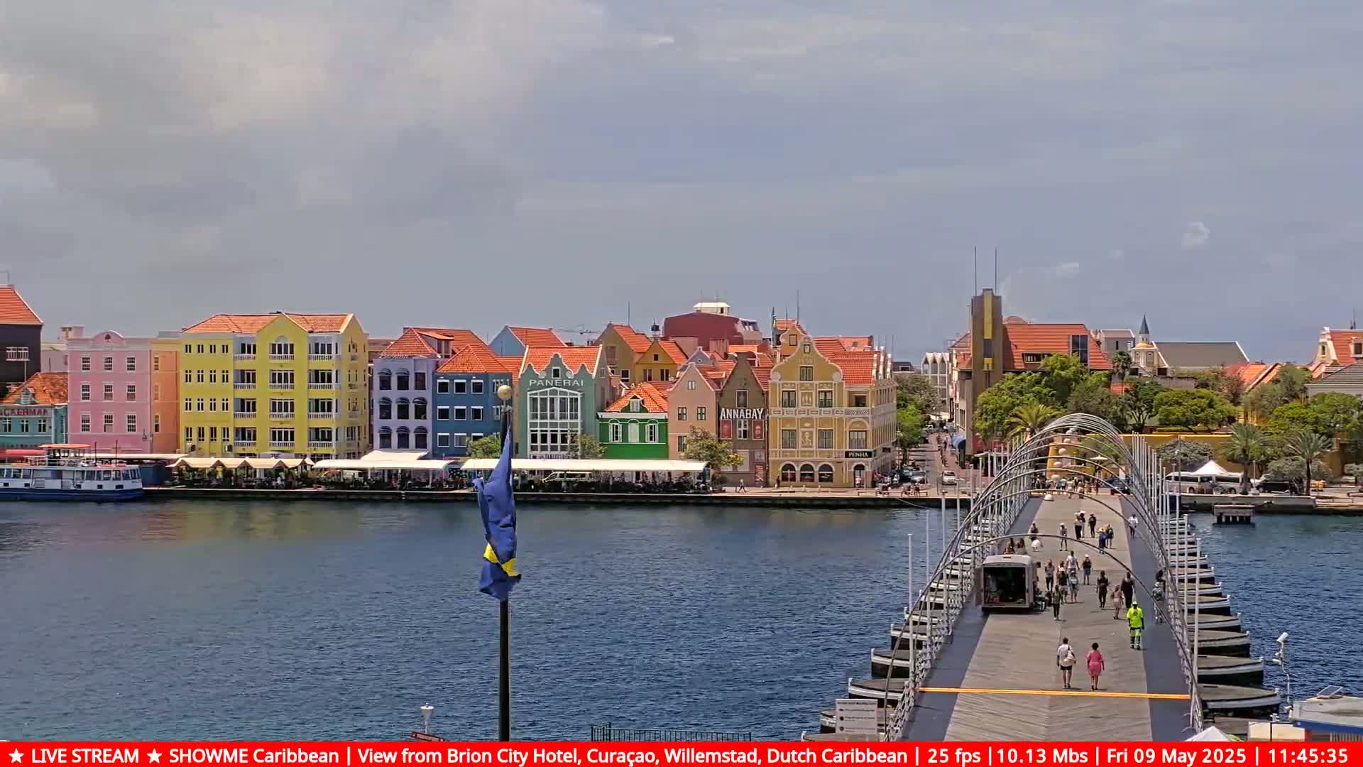 A pontoon bridge spans a waterway, with colorful buildings lining the waterfront under a partly cloudy sky.