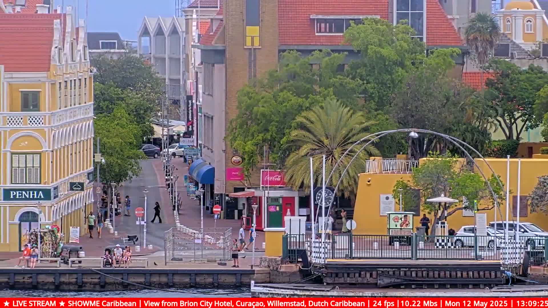 A waterfront scene shows a sunny day in a city with colorful colonial-style buildings, pedestrians, and a floating dock.