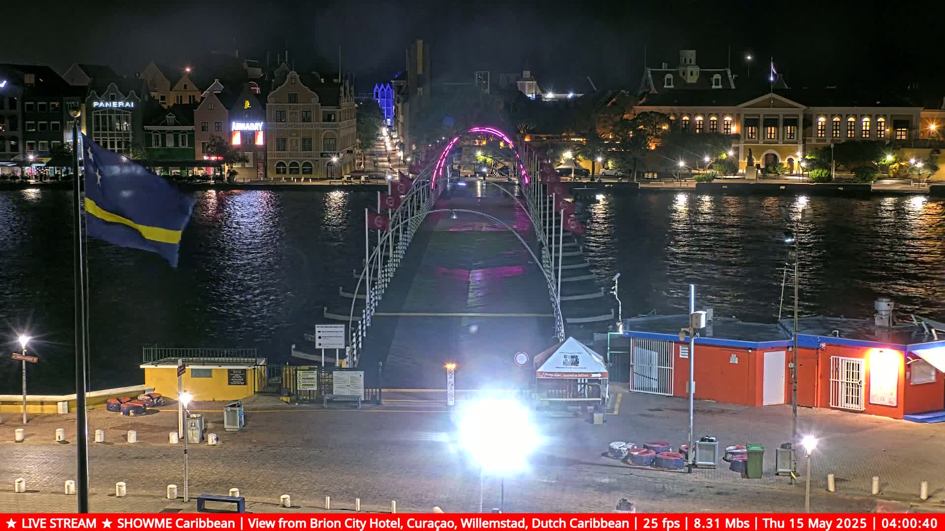 A brightly lit pontoon bridge spans a dark river at night, with colorful buildings lining the waterfront.