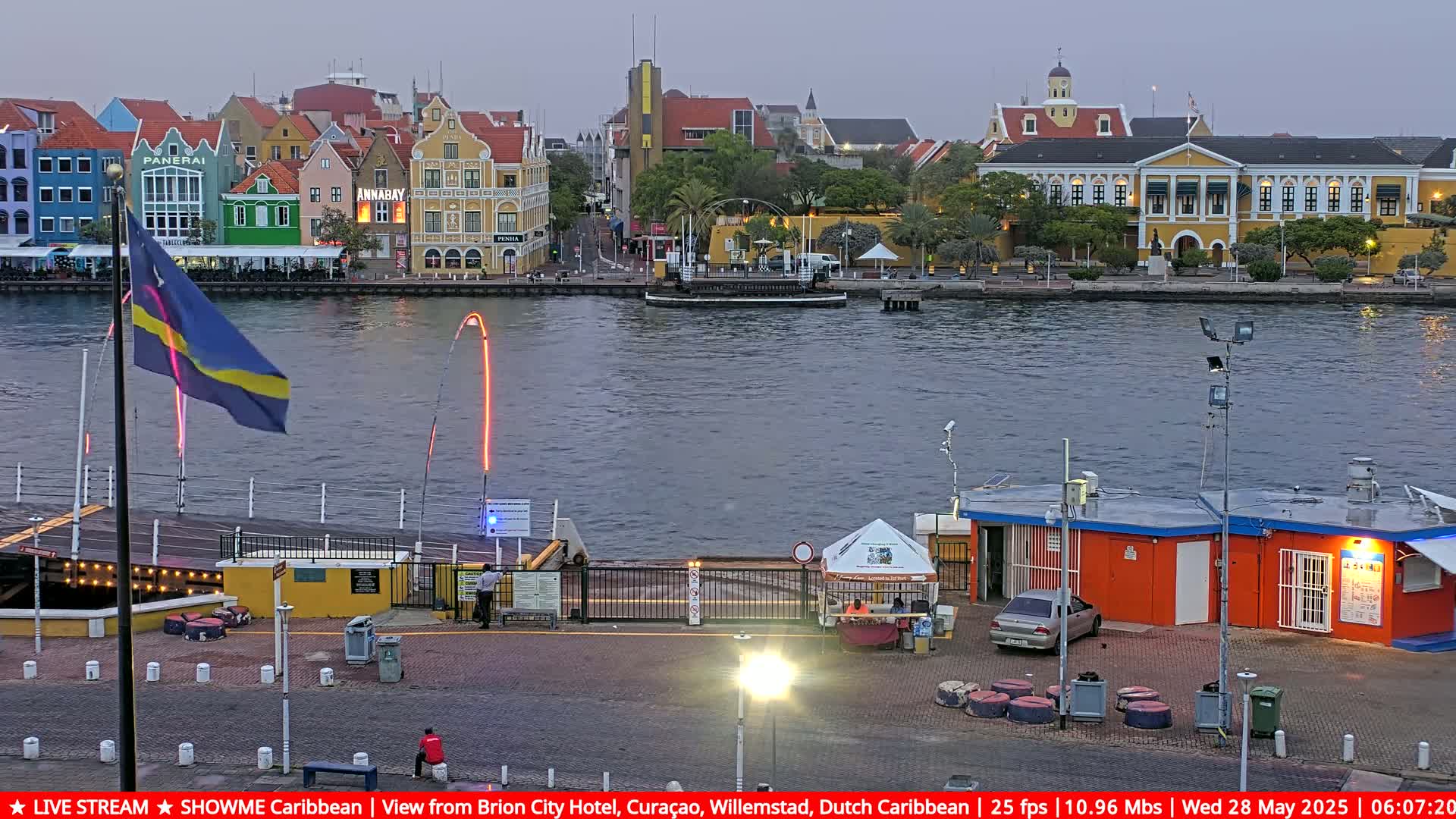 A waterfront scene at dusk shows colorful buildings lining a waterway, with a bridge partially open, a small boat in the water, and a flagpole displaying a flag.