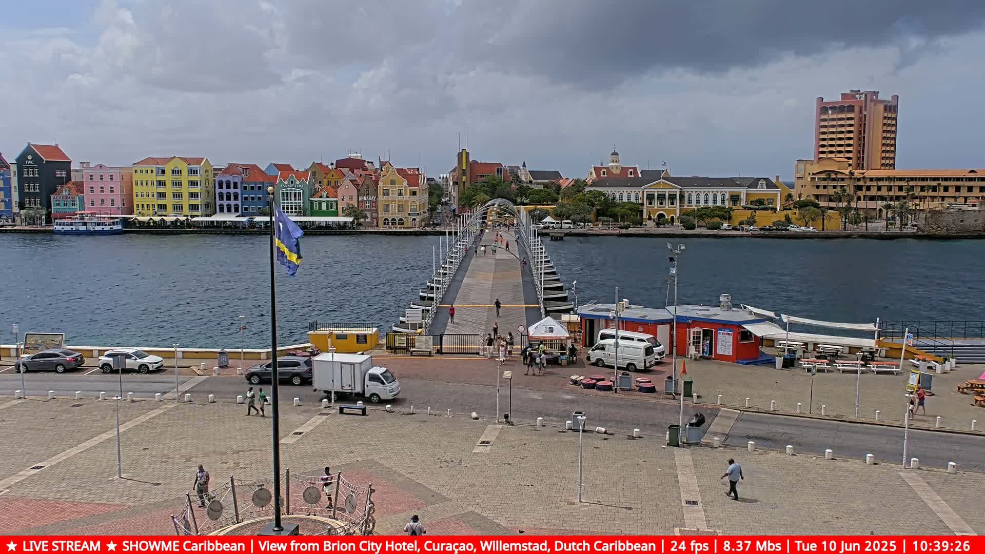 A pontoon bridge extends over a body of water toward colorful buildings under a partly cloudy sky.