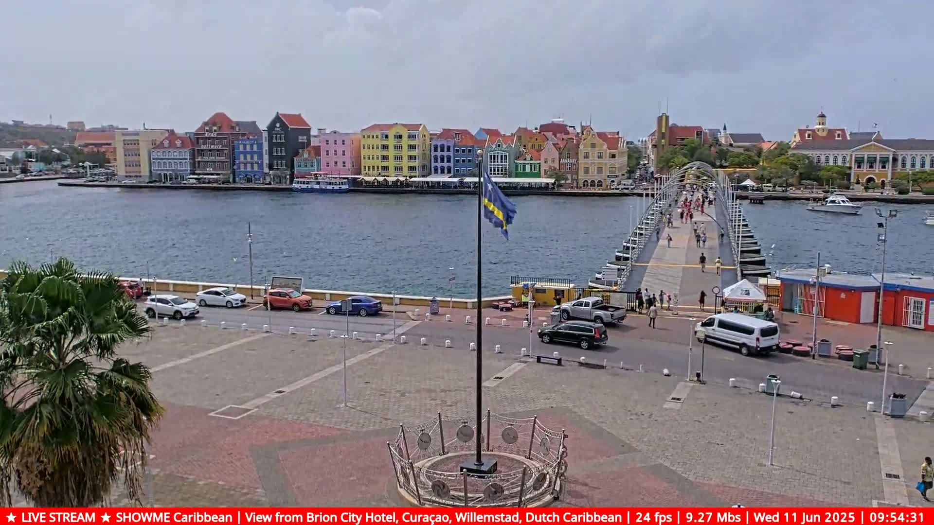 A pontoon bridge connects to a waterfront lined with colorful buildings under a partly cloudy sky.