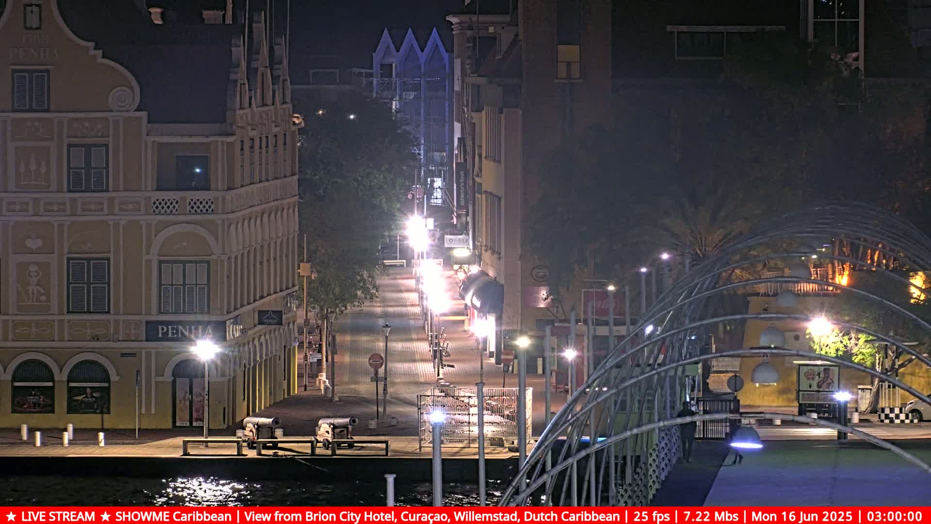 A nighttime view of a waterfront street scene, showing illuminated buildings and a walkway with sparsely populated areas.