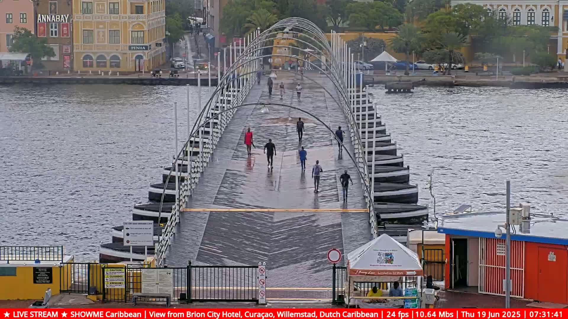 A pontoon bridge stretches across a waterway under a rainy sky, with several pedestrians walking across it.
