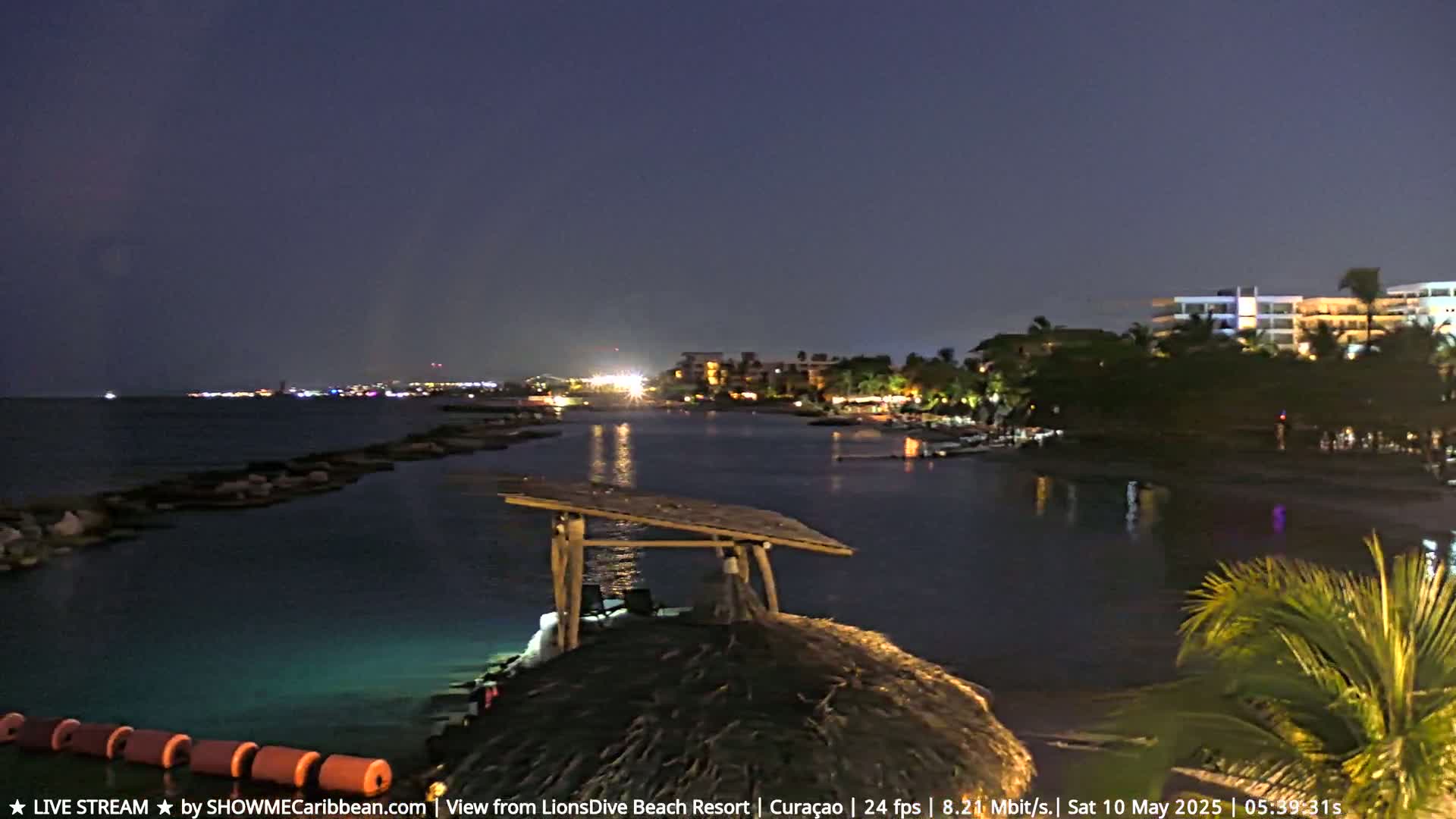 A nighttime view of a calm bay with a resort in the background, under a dark sky.
