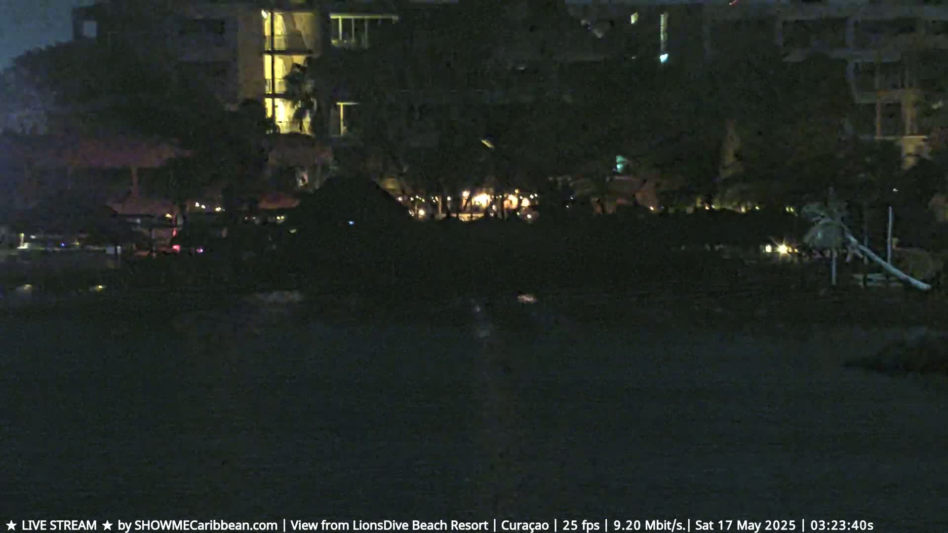 A nighttime view of a beach resort with dimly lit outdoor areas and a dark body of water.