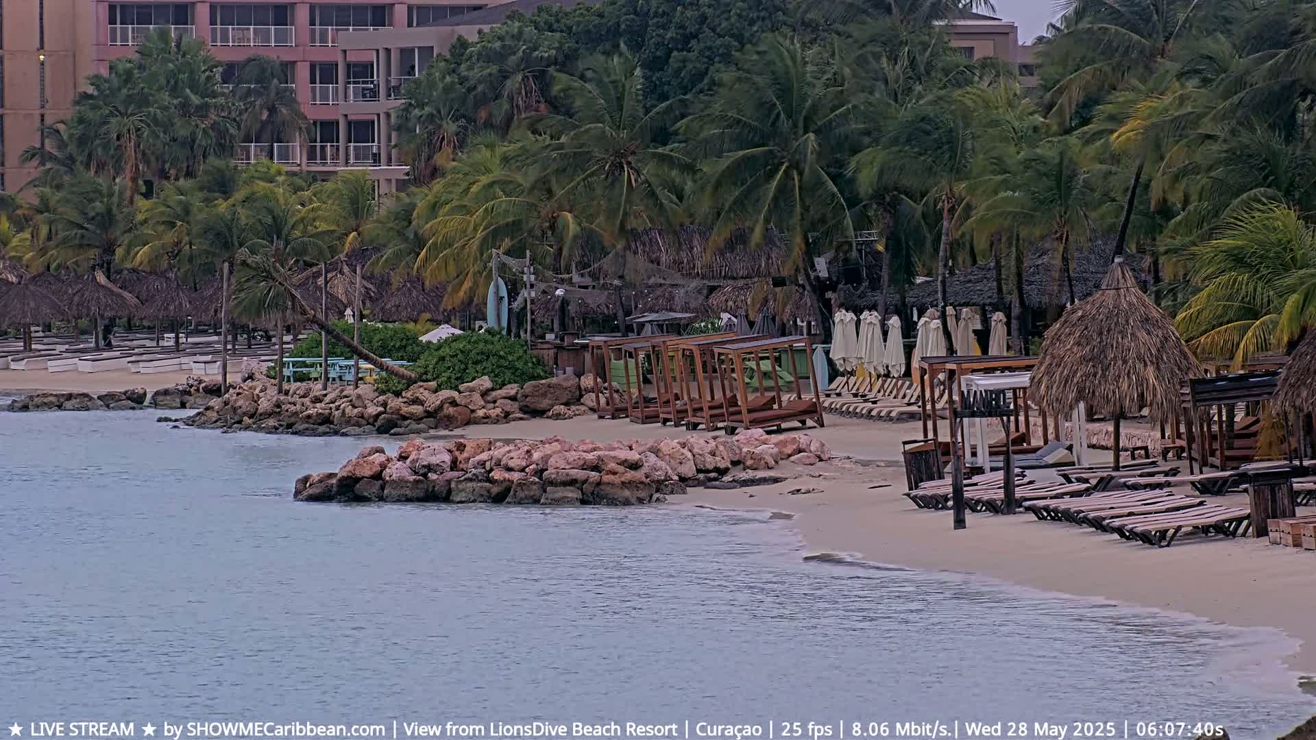 A tropical beach with palm trees, beach chairs, and cabanas is partially obscured by an overcast sky.
