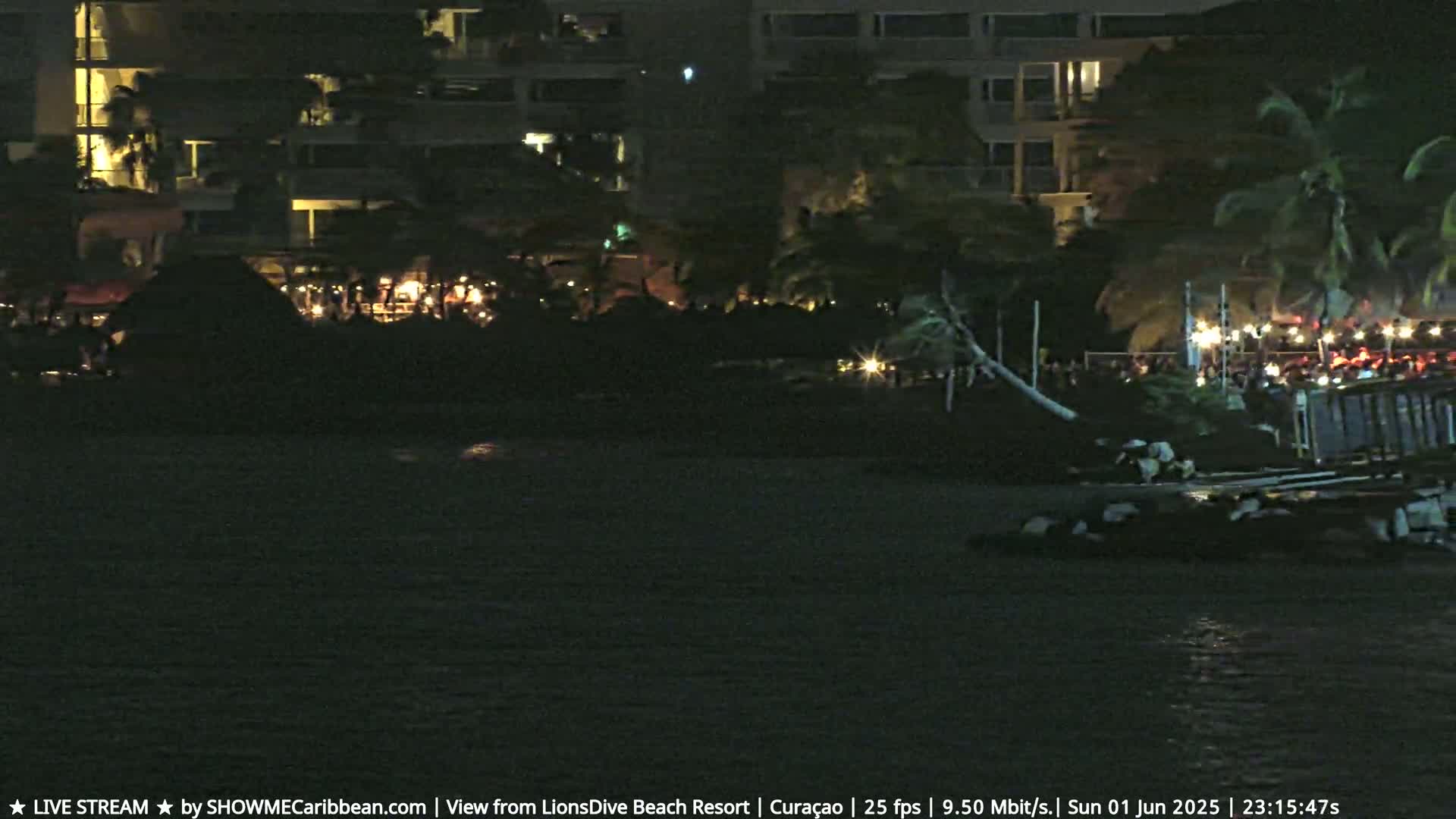 A nighttime view of a beach resort with lights illuminating the shoreline and a calm body of water.
