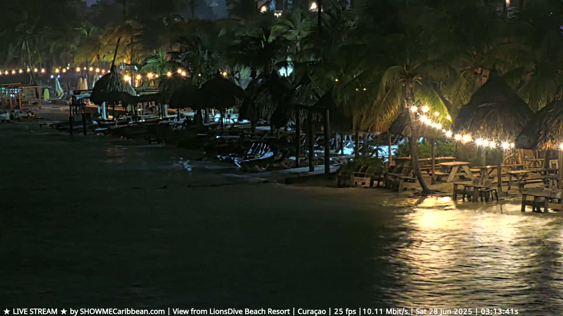 A nighttime beach scene shows several thatched-roof structures with string lights, picnic tables, and palm trees, partially submerged in dark, choppy water.