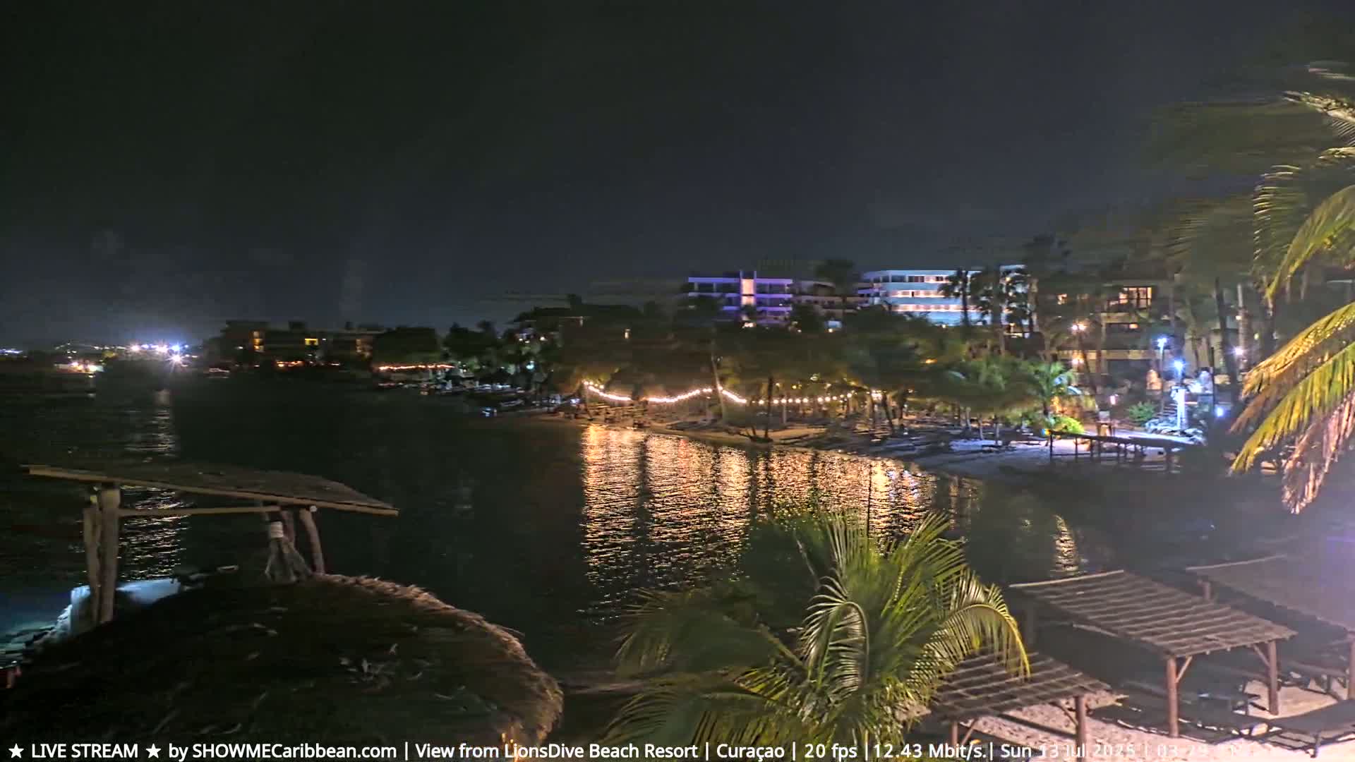A nighttime view of a calm body of water reflecting lights from a resort's beach area and buildings.