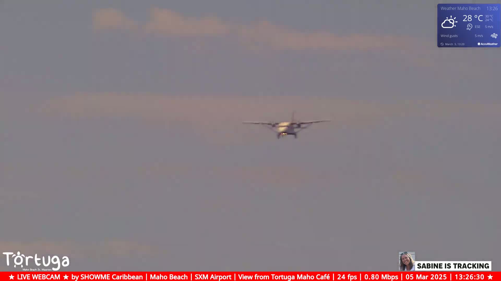 A small airplane is approaching the camera against a mostly cloudy, light-grey sky.