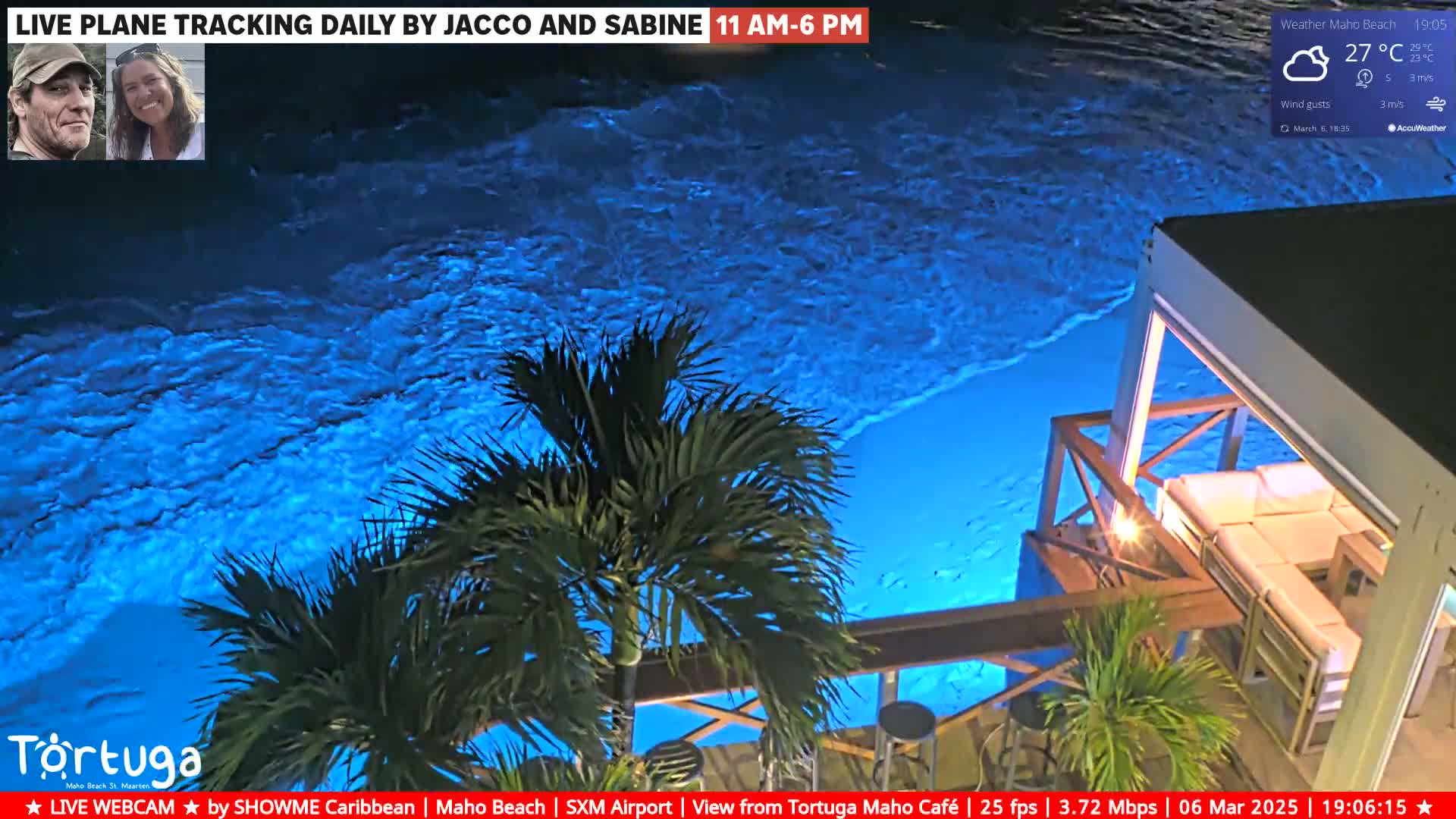 A nighttime view of a brightly lit blue ocean next to a patio with outdoor furniture, under partly cloudy skies.