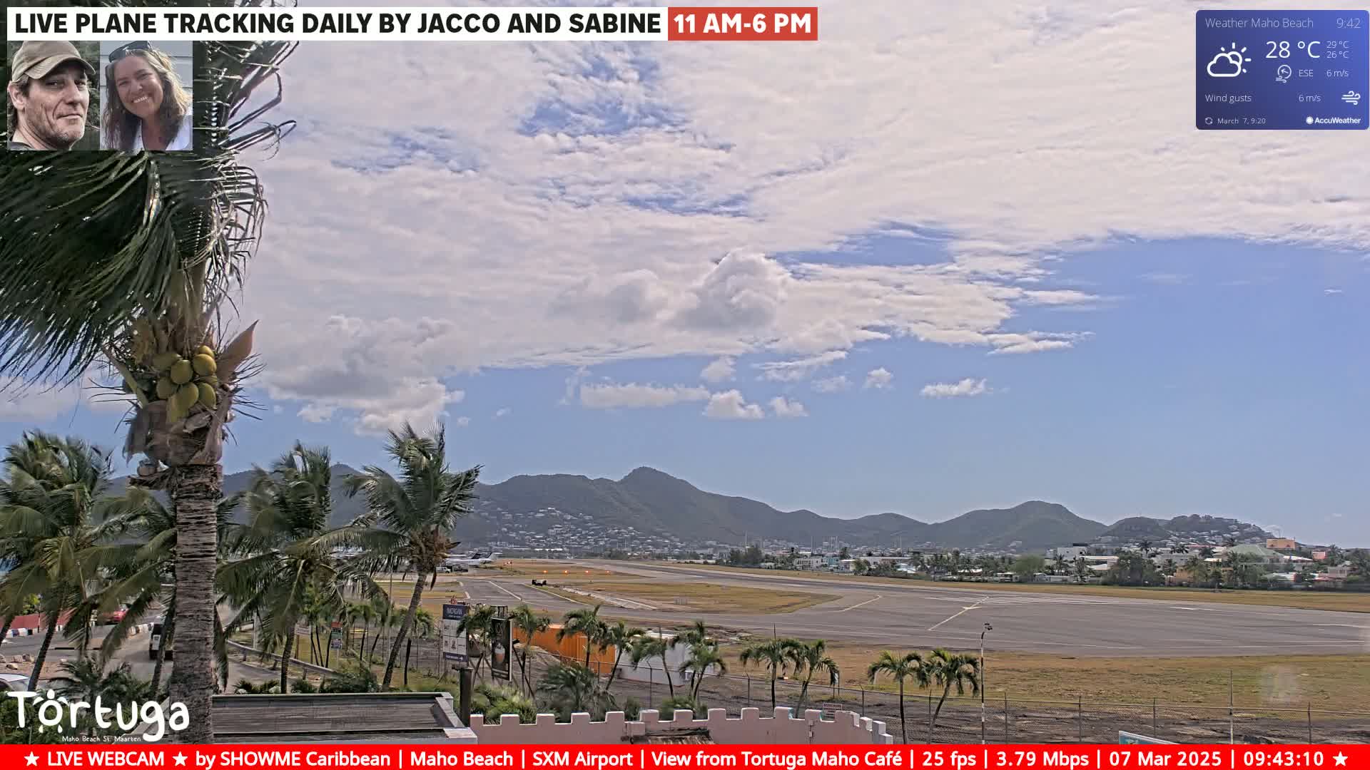 A partly cloudy sky overlooks an airport runway and surrounding palm trees, with mountains in the distance.