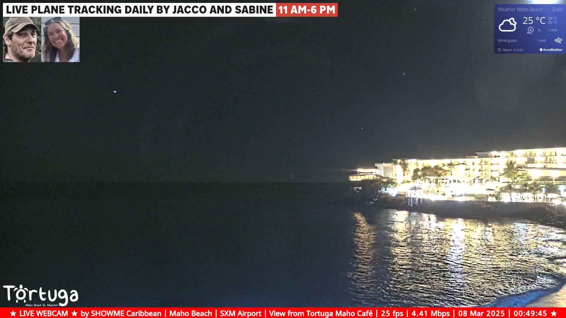 A nighttime seaside view shows a brightly lit resort along a dark shoreline under a partly cloudy sky.