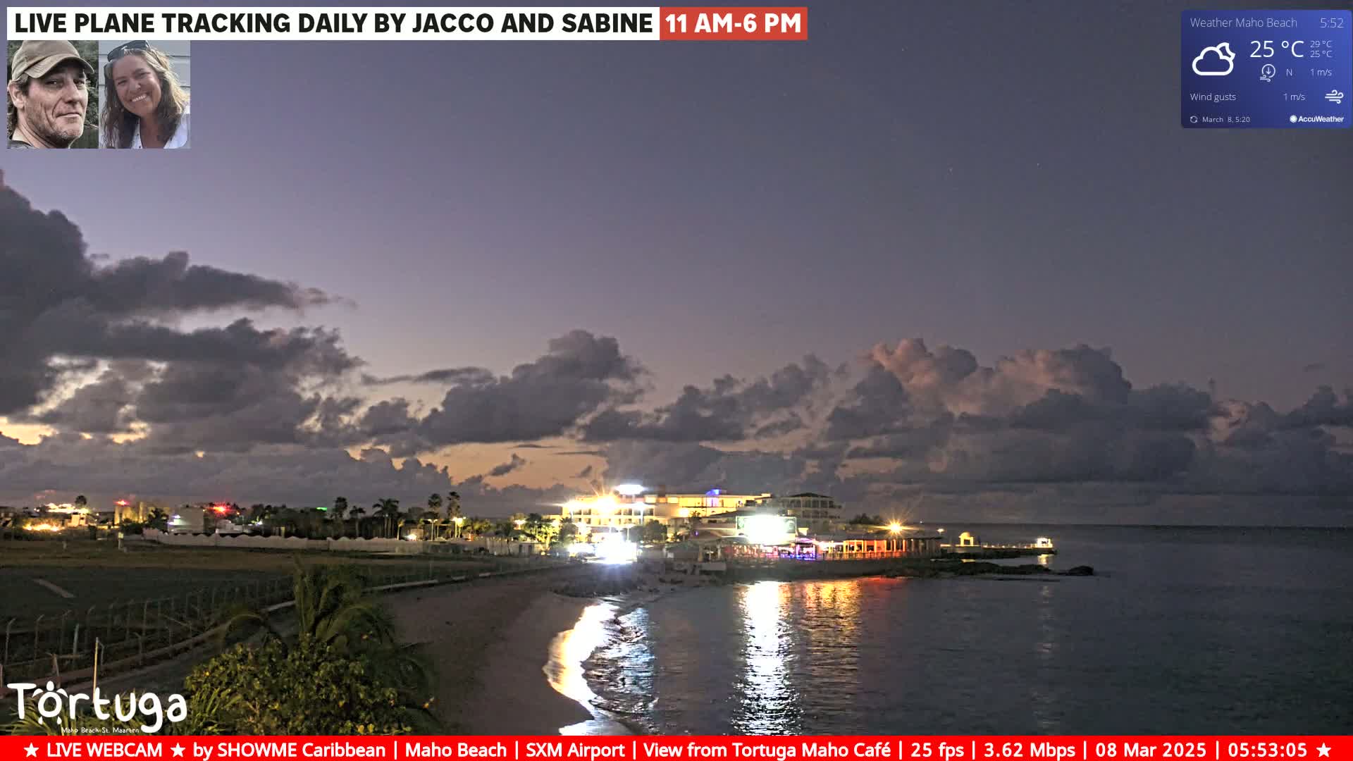 A twilight coastal scene shows a beach, lit buildings, and calm water under a partly cloudy sky.