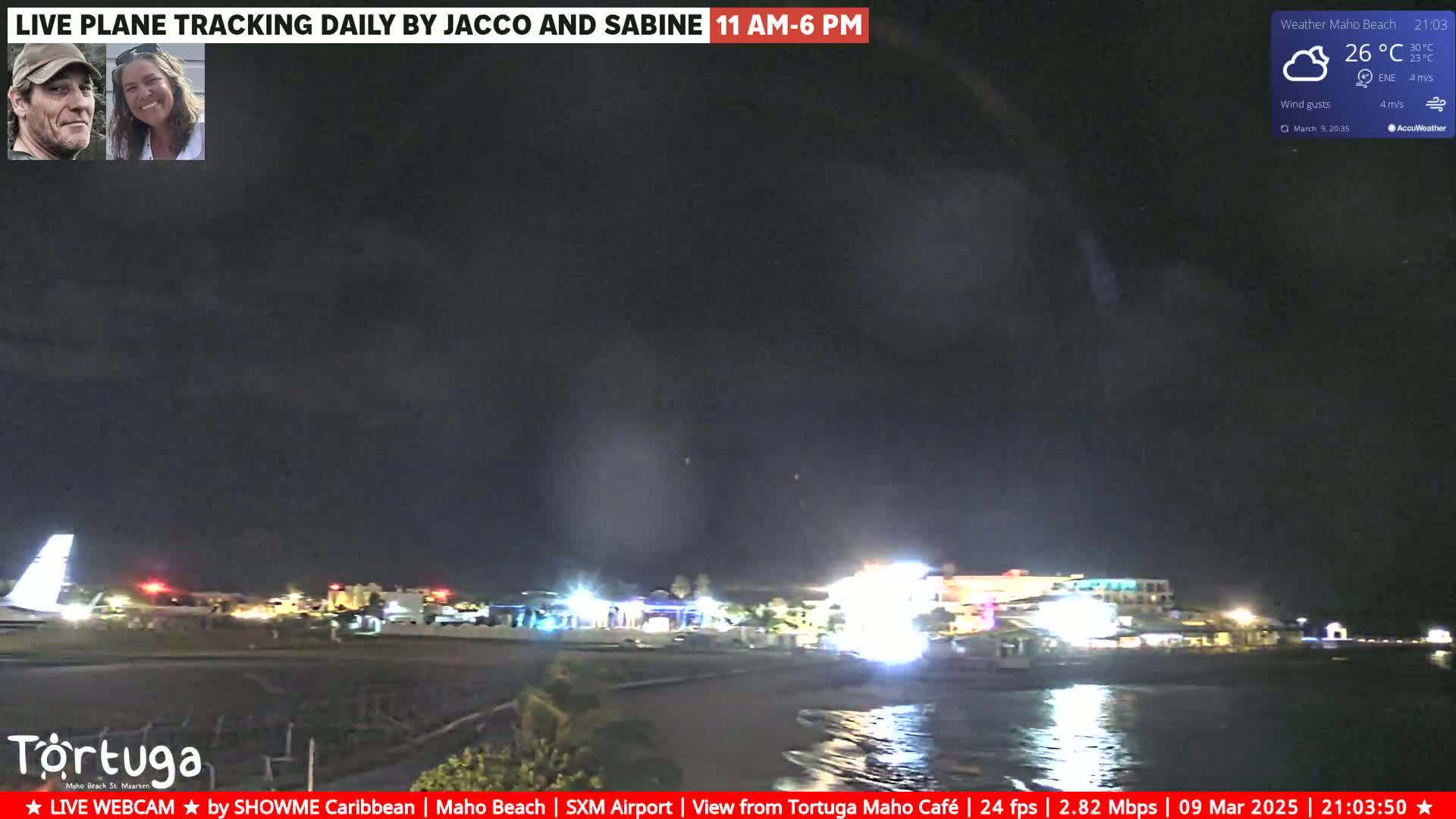 A nighttime coastal scene shows a dark, cloudy sky over a dimly lit beach and buildings near the water.
