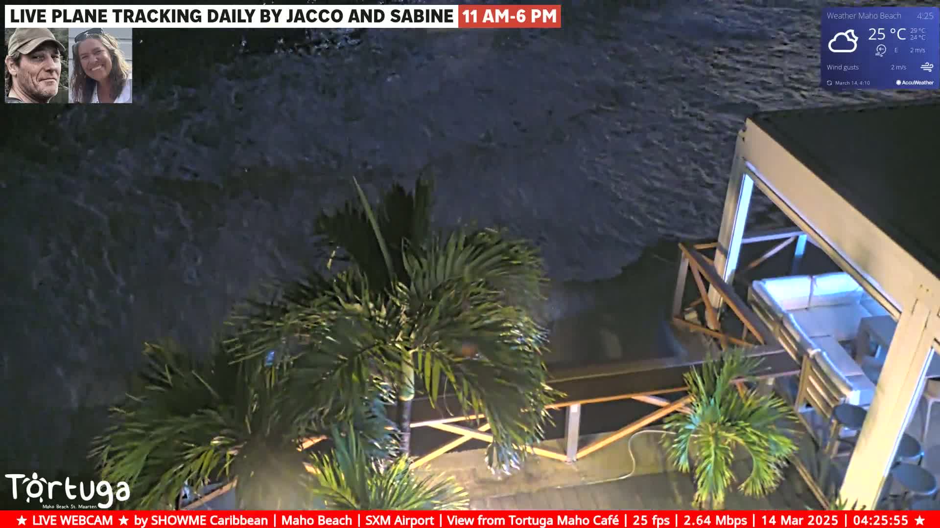 A nighttime, high-angle view shows dark, wavy water lapping against a patio with outdoor furniture and palm trees under a mostly cloudy sky.