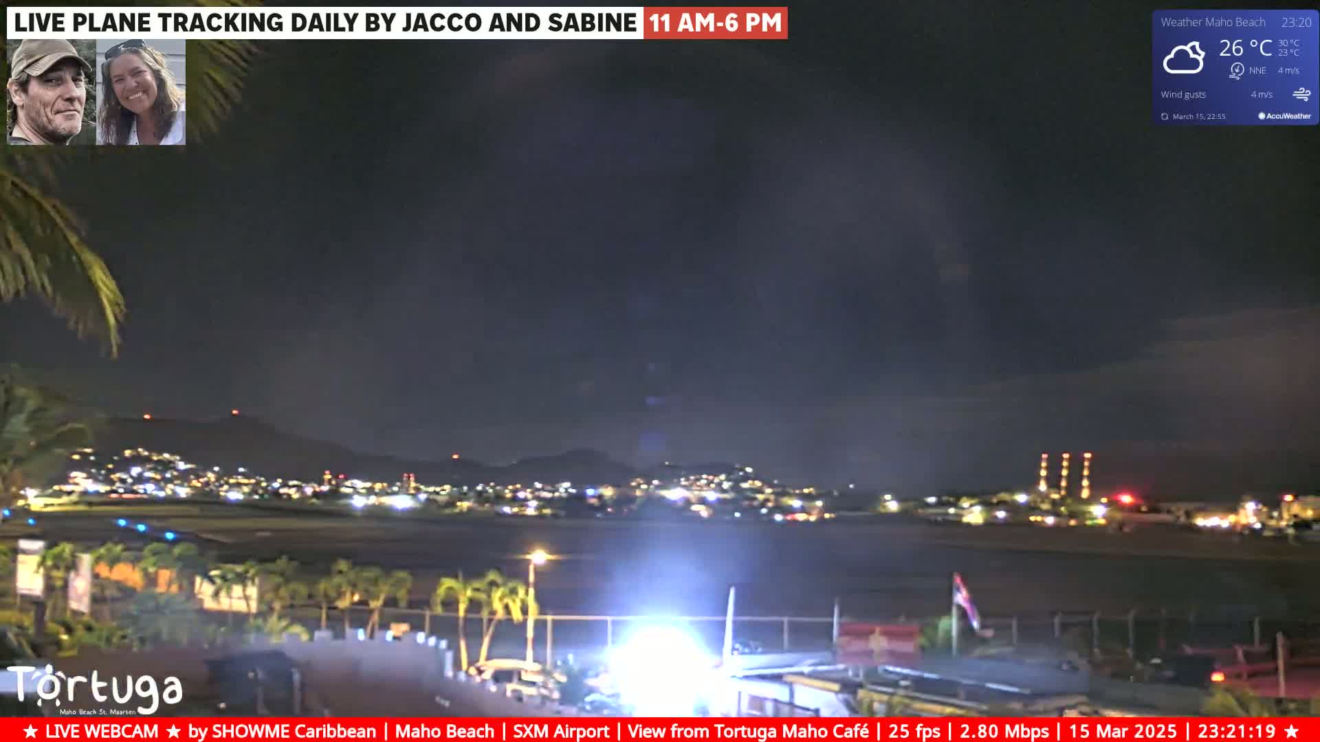 A nighttime view of an airport runway and surrounding city lights under a partly cloudy sky.