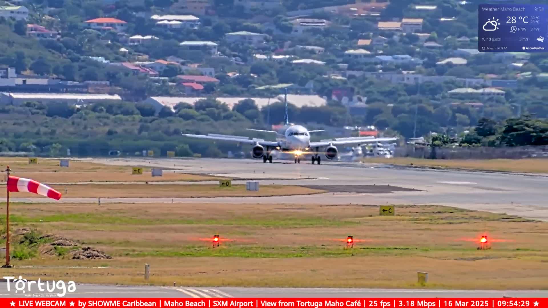 A passenger airplane is landing on a runway, with a partly sunny sky and light wind visible in the background, overlooking a residential area.