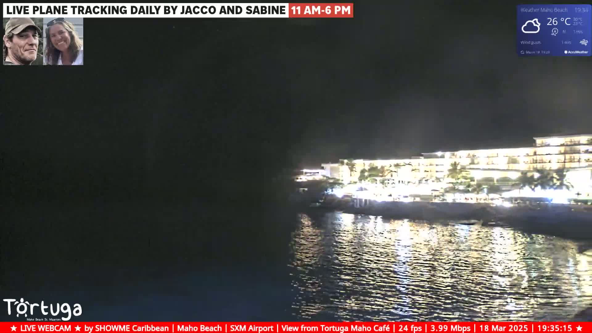 A nighttime, slightly cloudy view of a brightly lit beachfront hotel across a calm body of water.