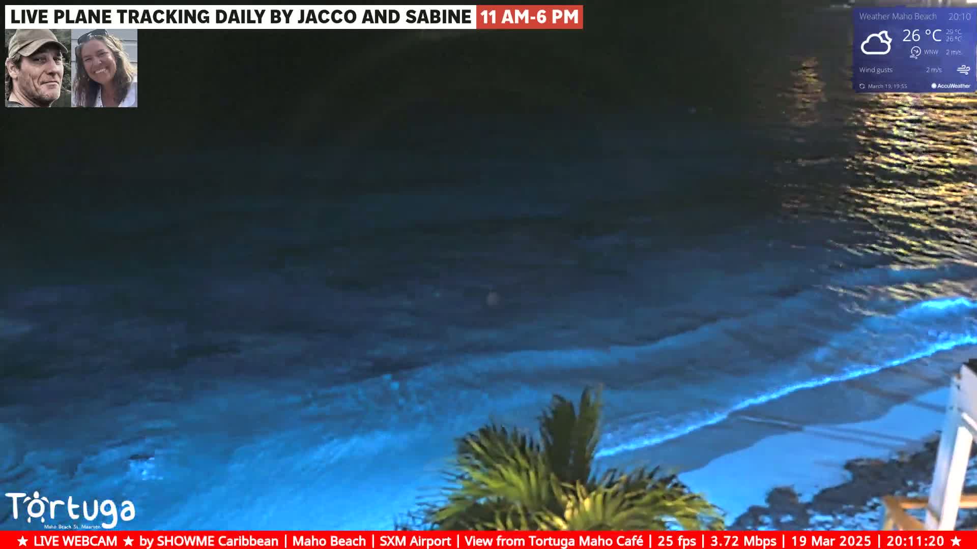 A nighttime ocean waves illuminated with bioluminescence wash ashore on a beach under partly cloudy skies.