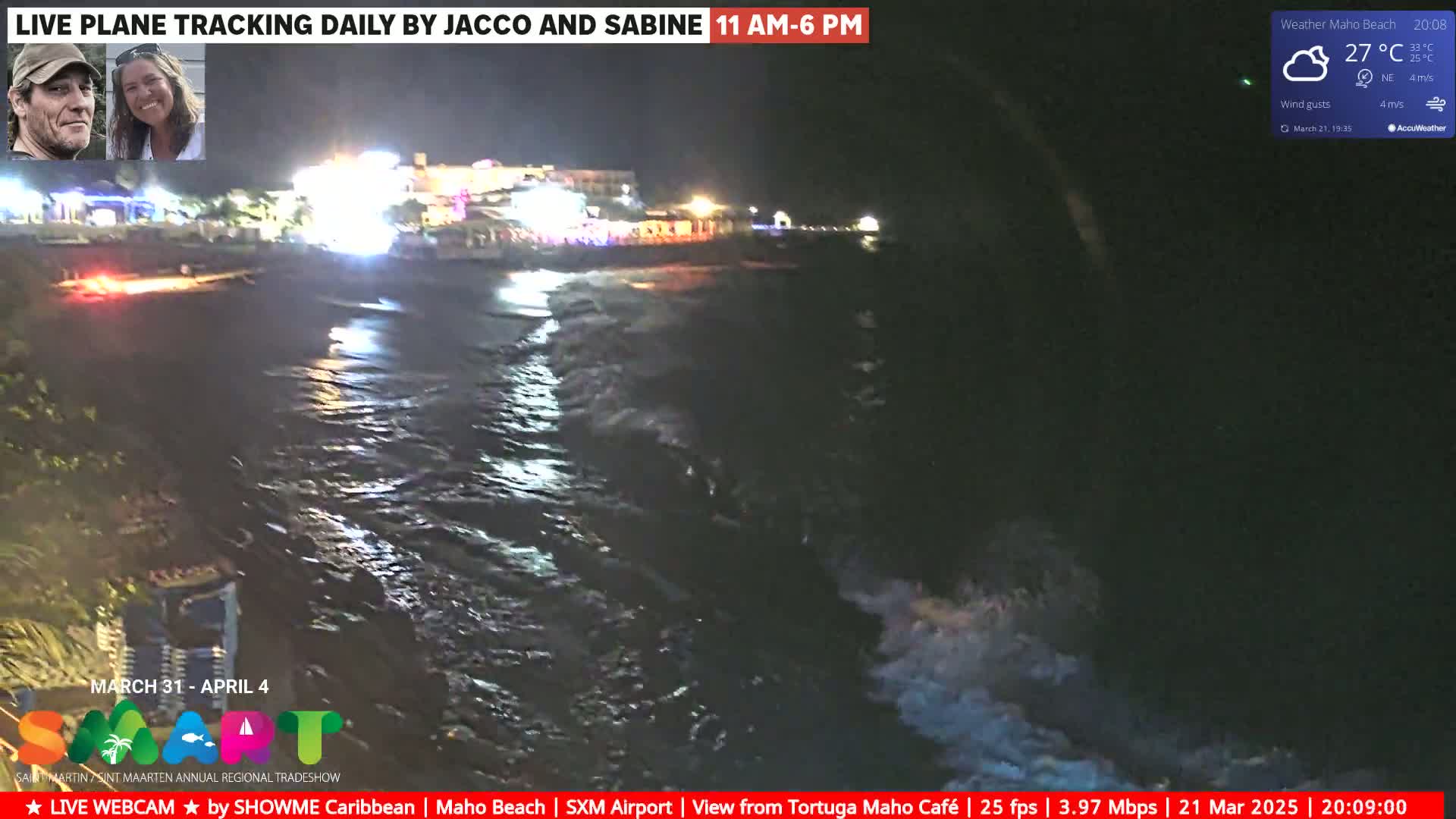 A nighttime beach scene shows dark, wavy water lapping at a shore with illuminated buildings in the background under a partly cloudy sky.