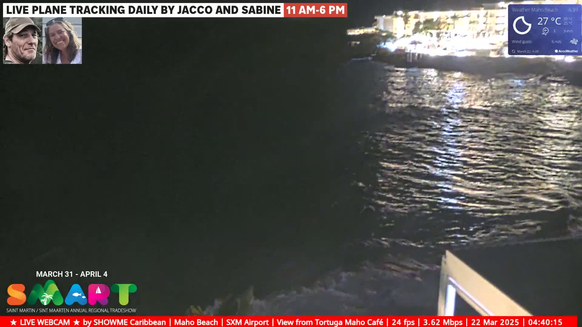 A nighttime view of a dark ocean with gentle waves lapping against a shore, illuminated by lights from buildings on the coast under a clear sky.