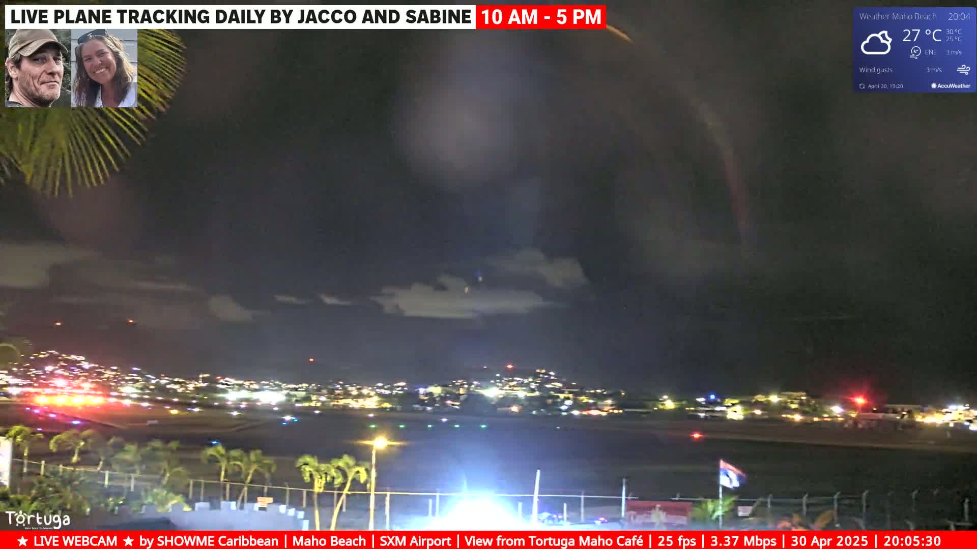 A nighttime view of an airport runway and surrounding city lights under a partly cloudy sky.