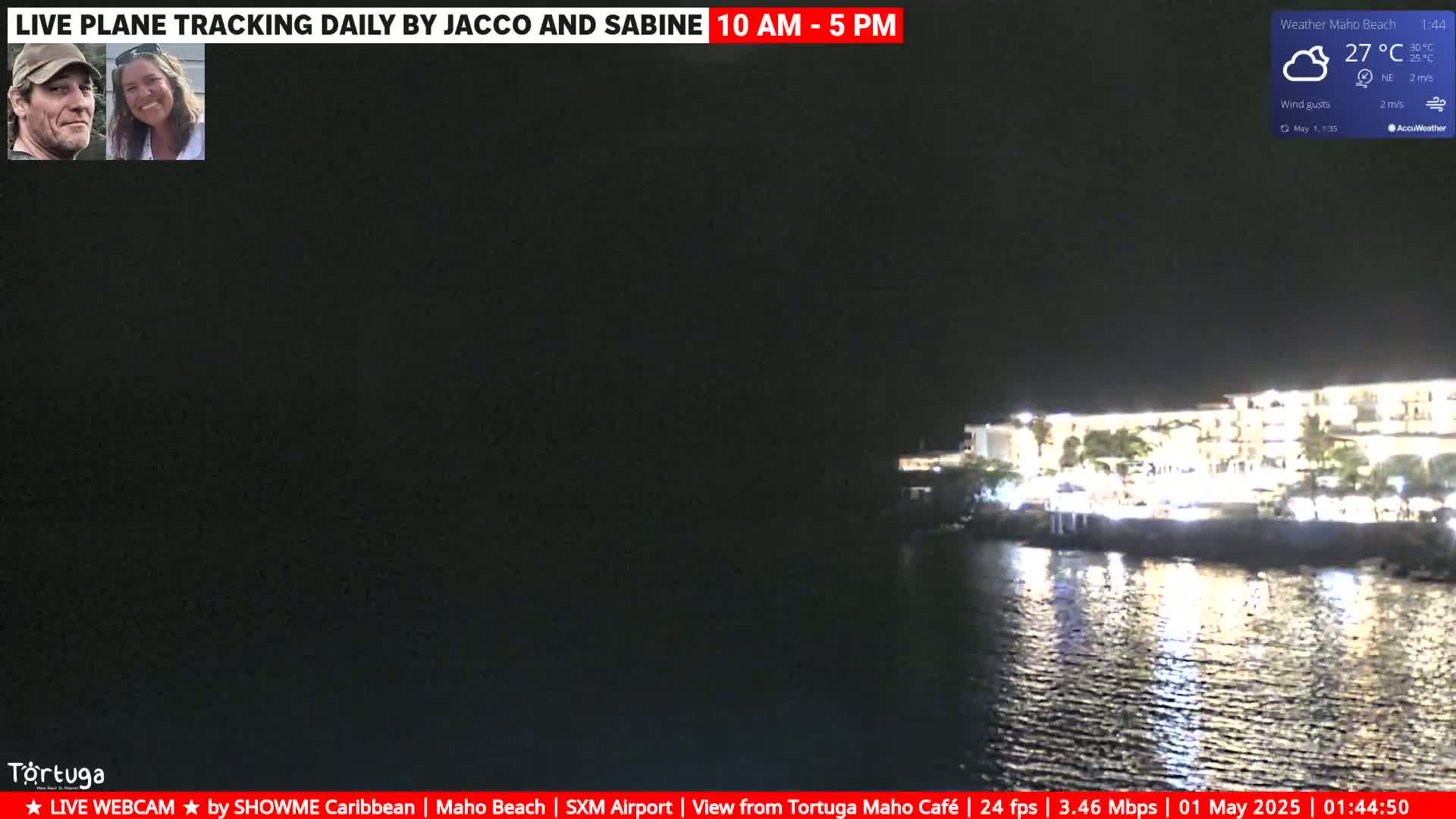 A nighttime view of a brightly lit building along a dark body of water under partly cloudy skies.
