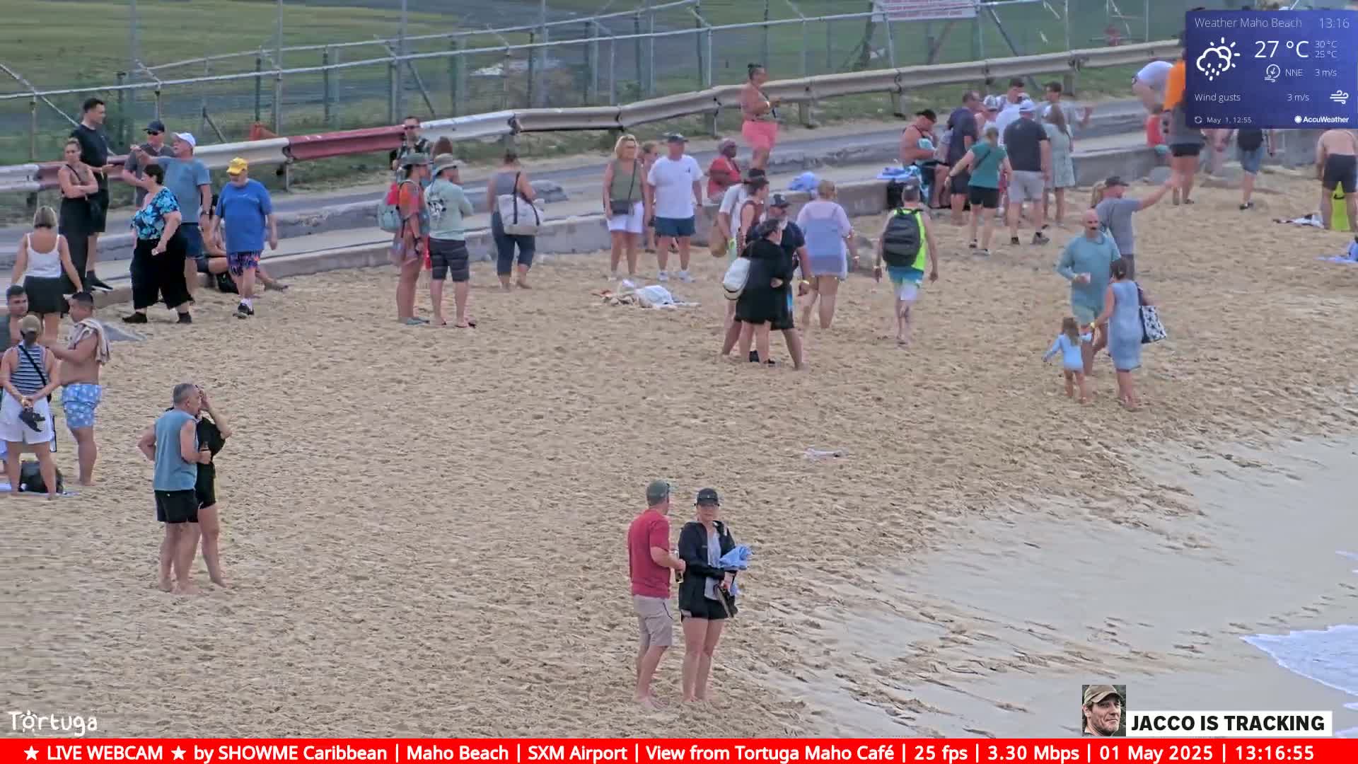 Many people are gathered on a sandy beach on a partly cloudy day with light winds.