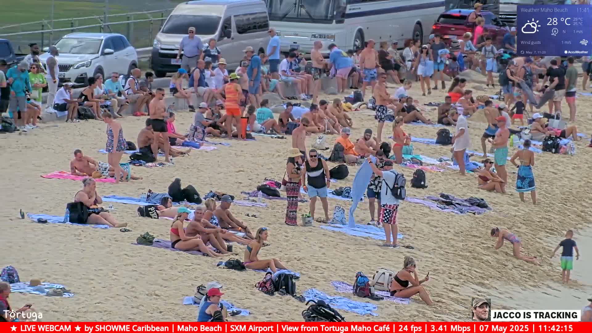 A sandy beach is crowded with people sunbathing, swimming, and relaxing under partly sunny skies.