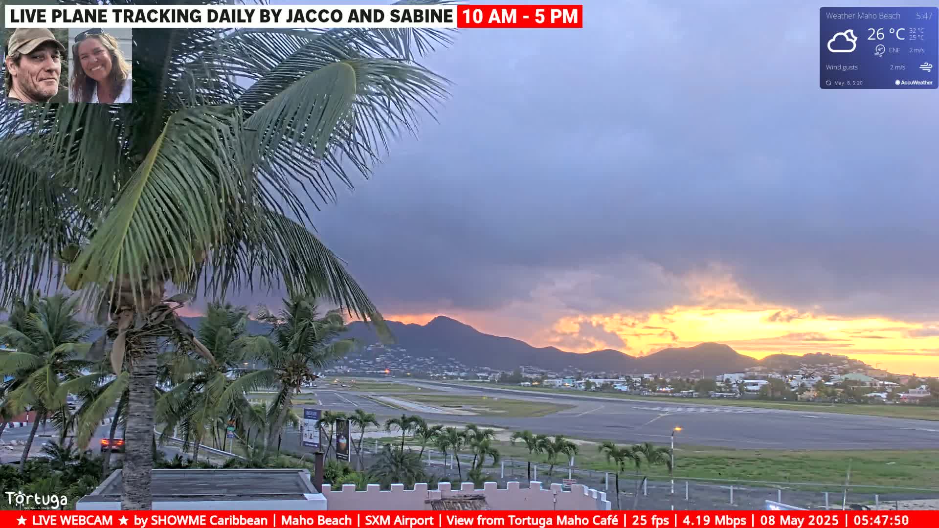 A partly cloudy sunset over an airport runway is seen from behind palm trees, with the sky showing a mix of gray and yellow-orange hues.
