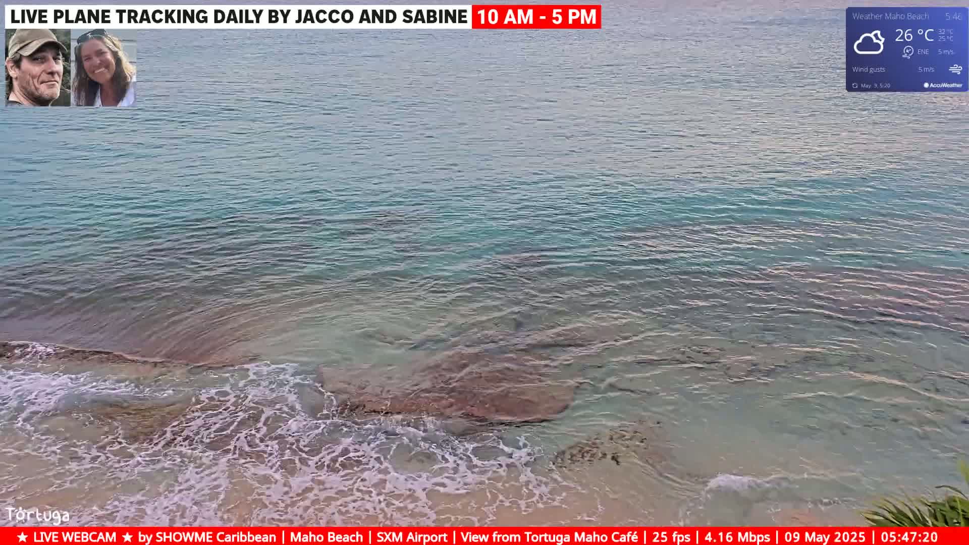 Clear, shallow turquoise water laps gently against a sandy shore under partly cloudy skies.