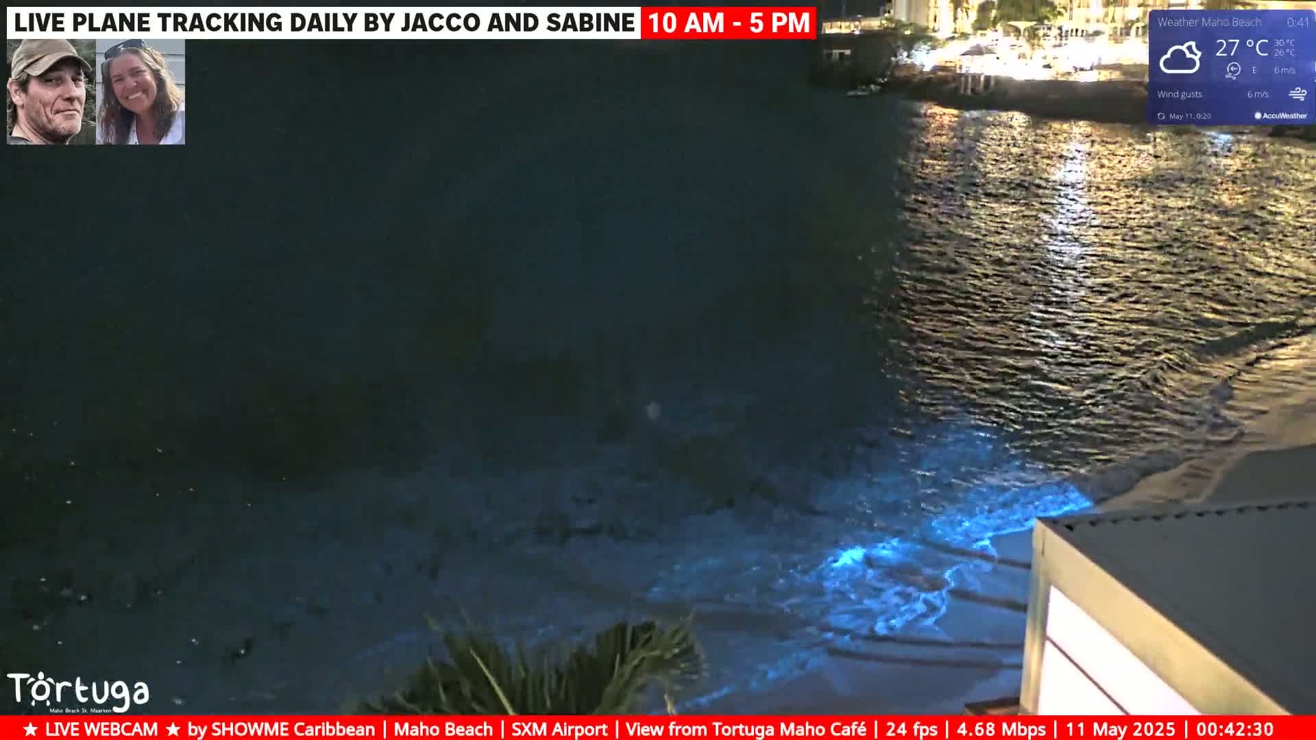 A nighttime view of bioluminescent waves lapping a sandy shore under partly cloudy skies.