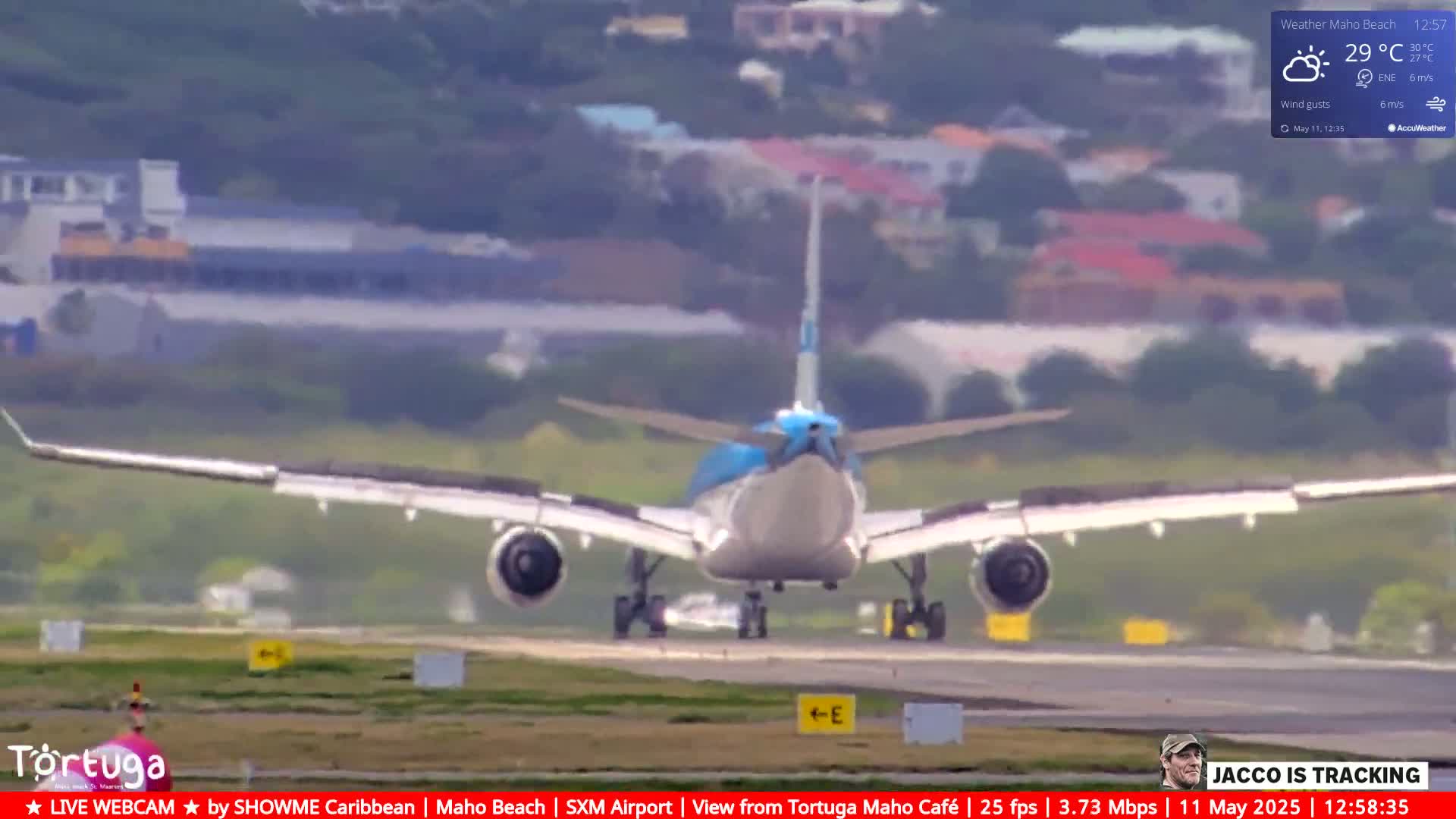 A large airplane is landing on a runway on a partly sunny day with a light wind.