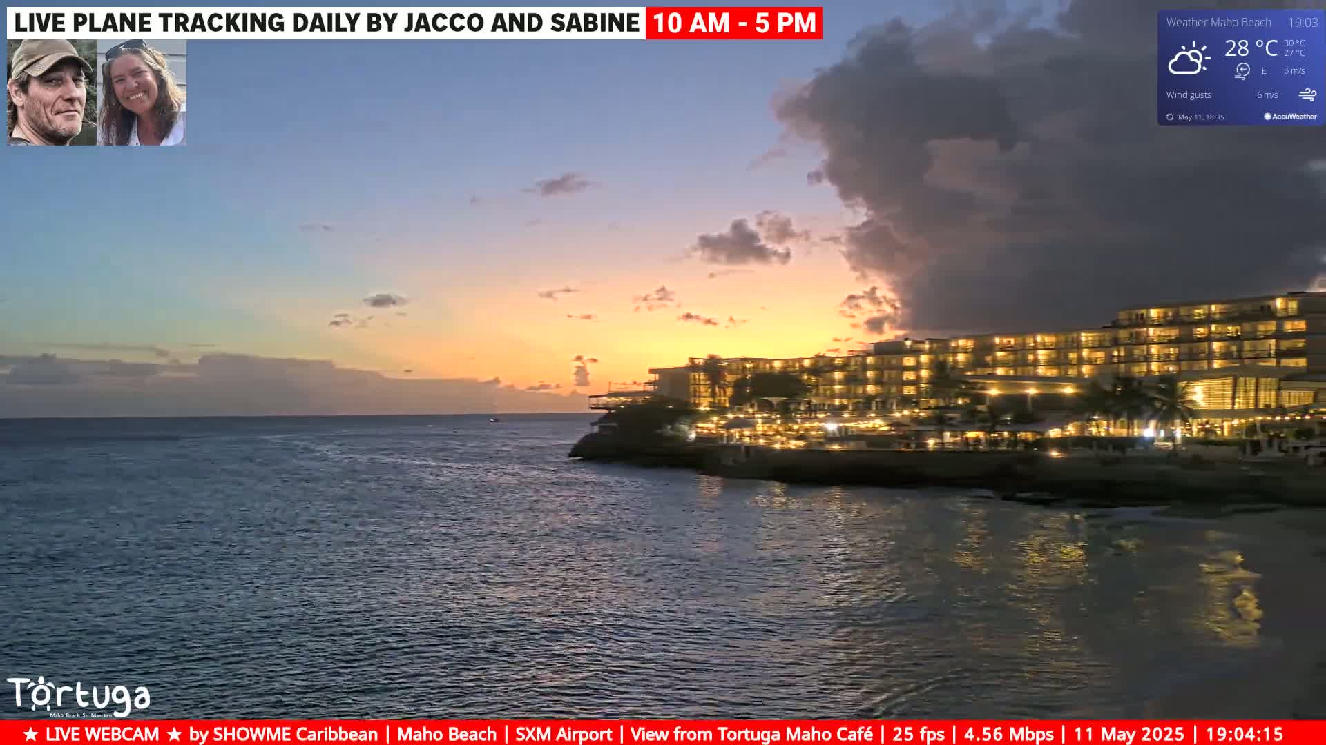A brightly lit resort sits on a rocky shoreline at sunset, under a partly cloudy sky with wind gusts.