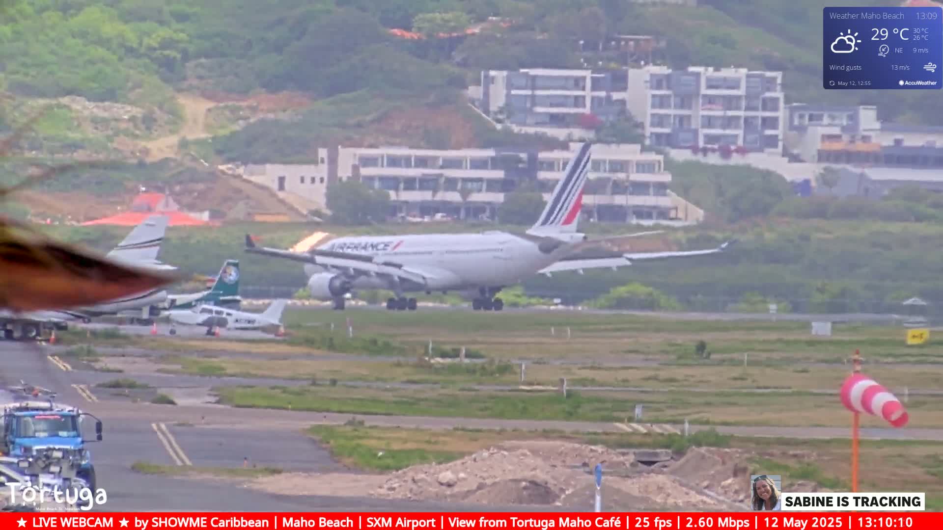 A large Air France airplane is landing on an airport runway on an overcast day, with smaller planes and airport vehicles visible in the foreground.