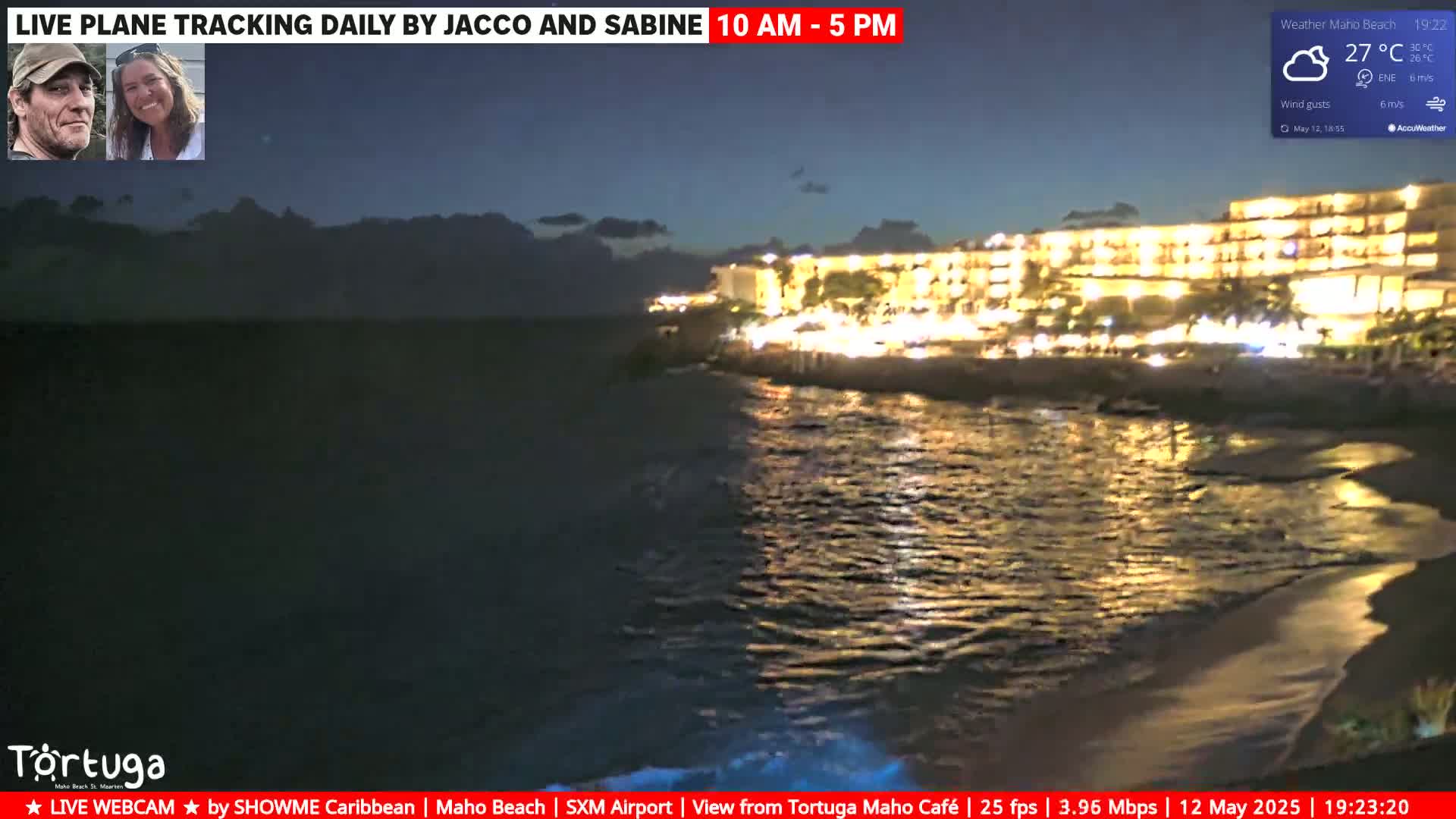 A brightly lit beachfront resort is seen at night, under a partly cloudy sky, next to a dark body of water with small waves.