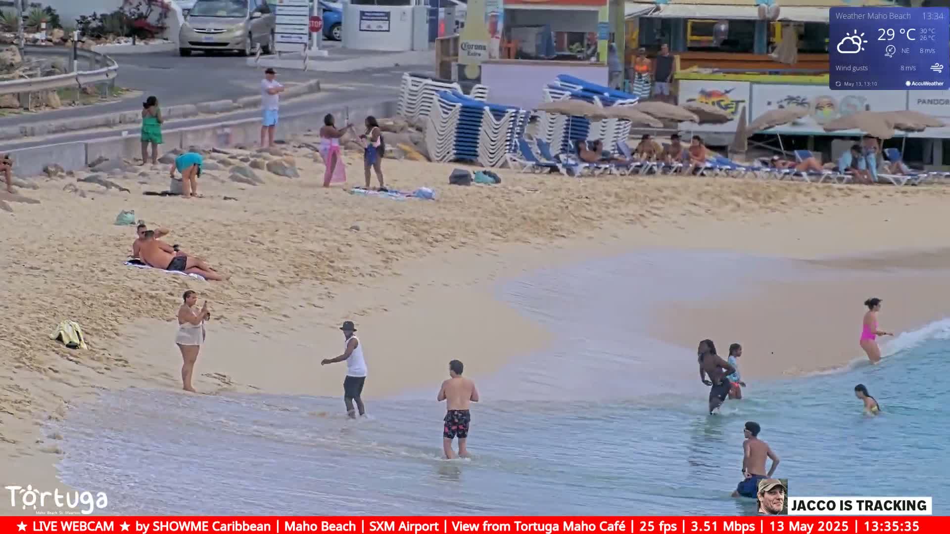 A sunny beach scene shows people relaxing and swimming in the ocean under partly cloudy skies.