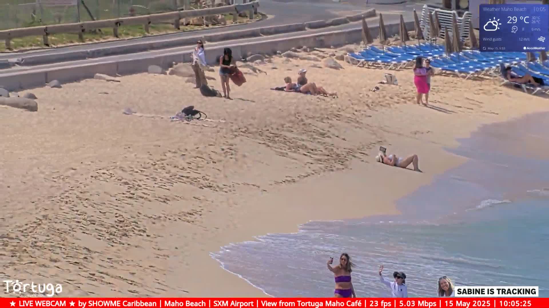 A sandy beach with several people sunbathing and walking along the shore on a sunny day with light winds.