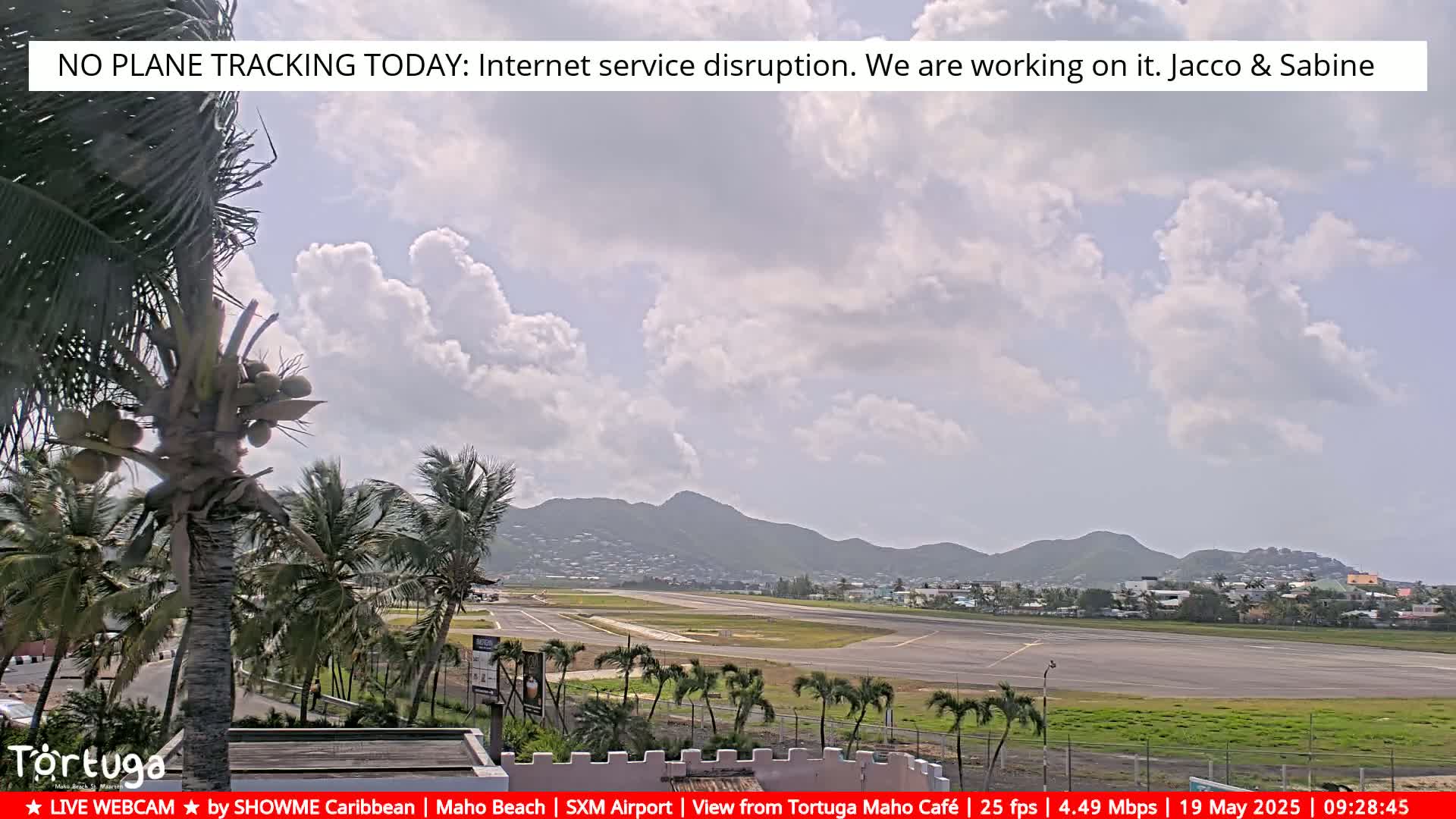 A partly cloudy day reveals an airport runway and surrounding palm trees, with hills in the background.