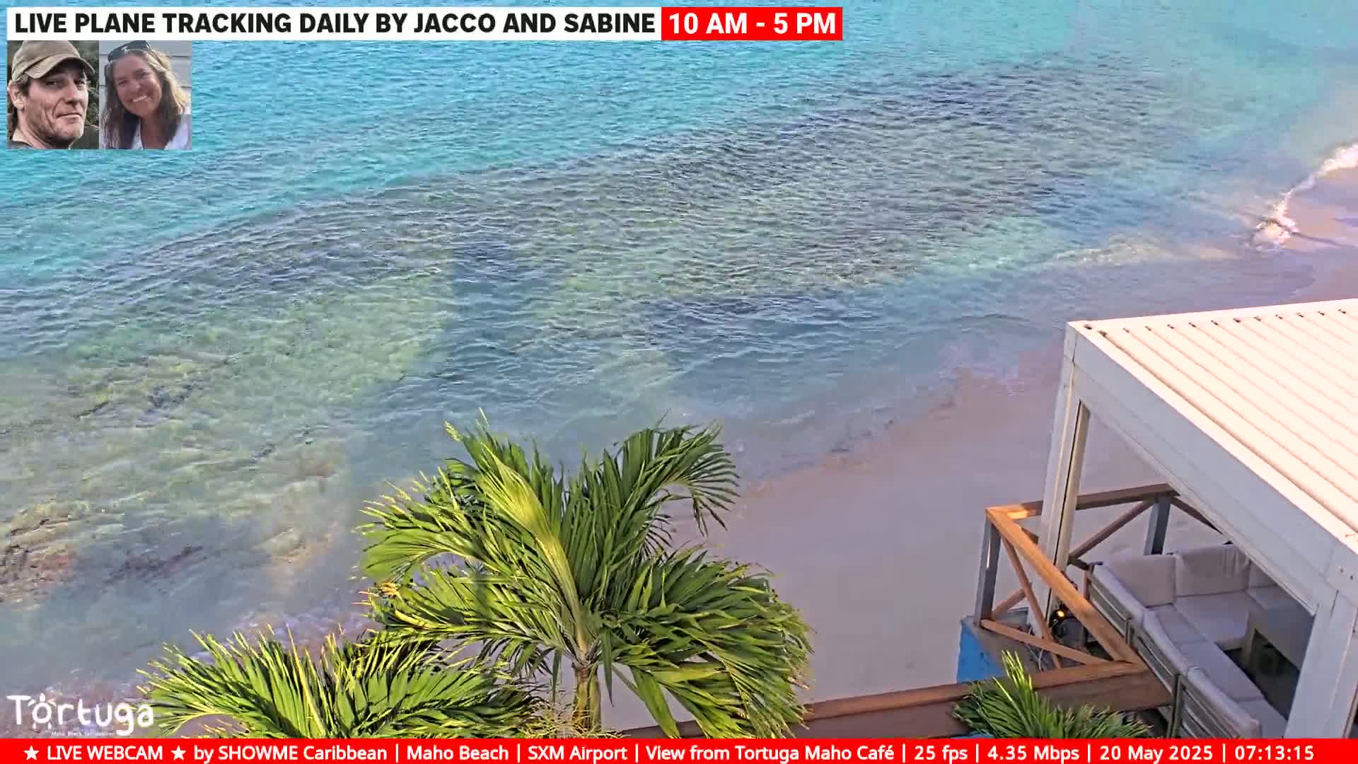Clear, turquoise water laps a sandy beach near a partially visible outdoor cafe with a white awning.