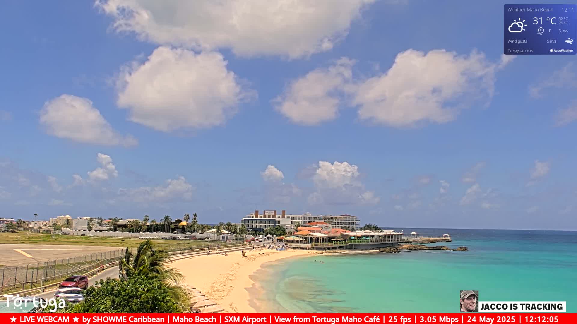 A sandy beach with turquoise water and a few buildings is visible under a partly cloudy sky.