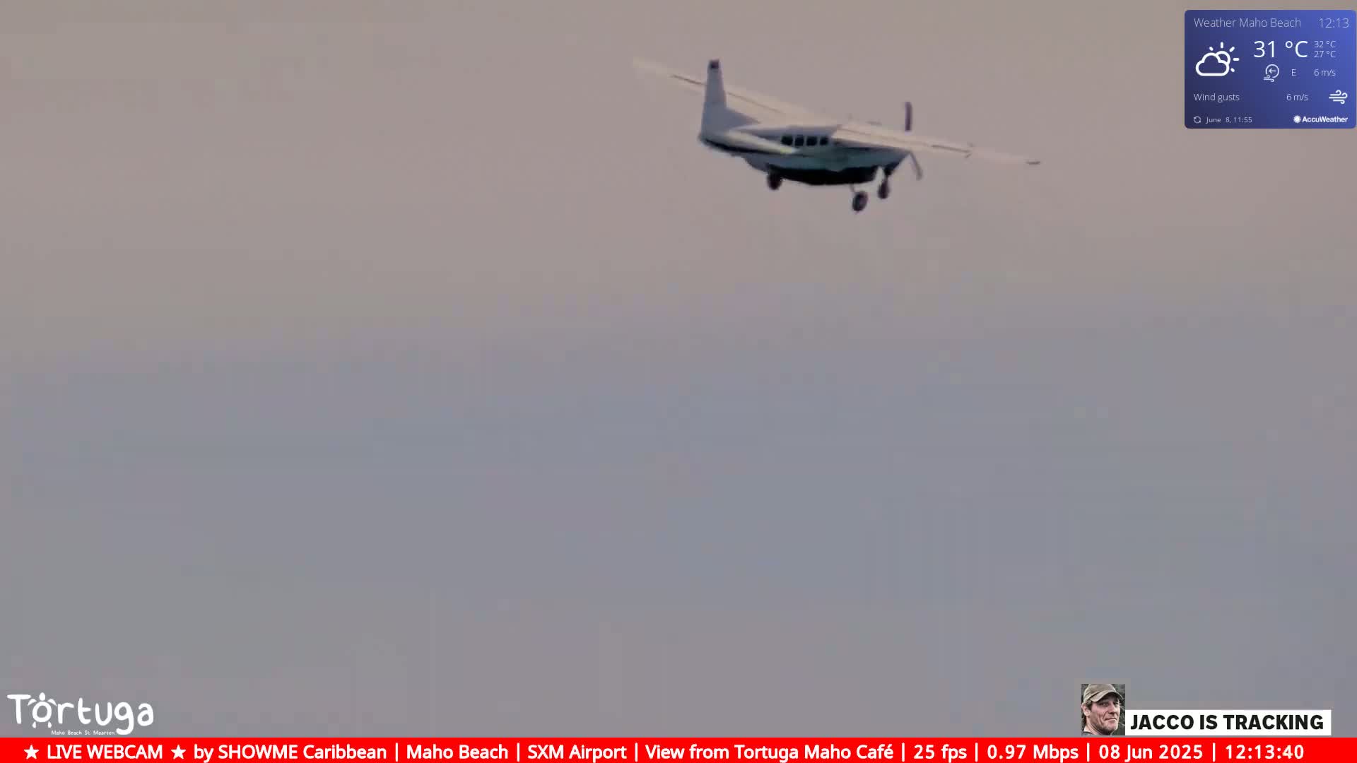 A small airplane flies through a hazy, light-grey sky under partly sunny conditions.