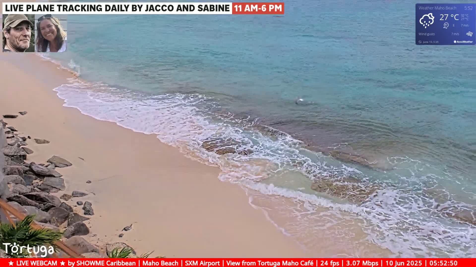 A sandy beach with light-colored sand and small rocks on the left, bordered by turquoise water with small waves breaking on the shore under partly cloudy skies.